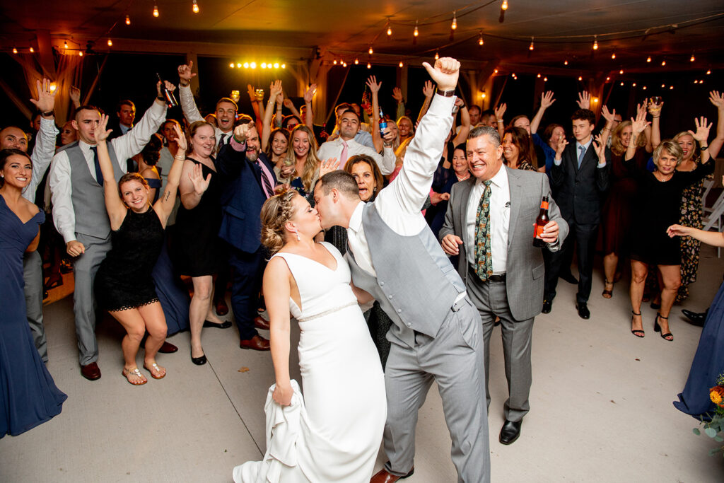 Bride and groom kiss in the middle of dance floor with guests around them