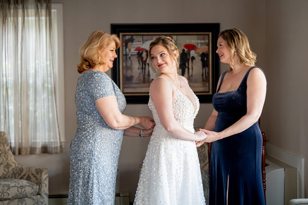 bride's mom and sister help her into her wedding dress at the Chocksett Inn.