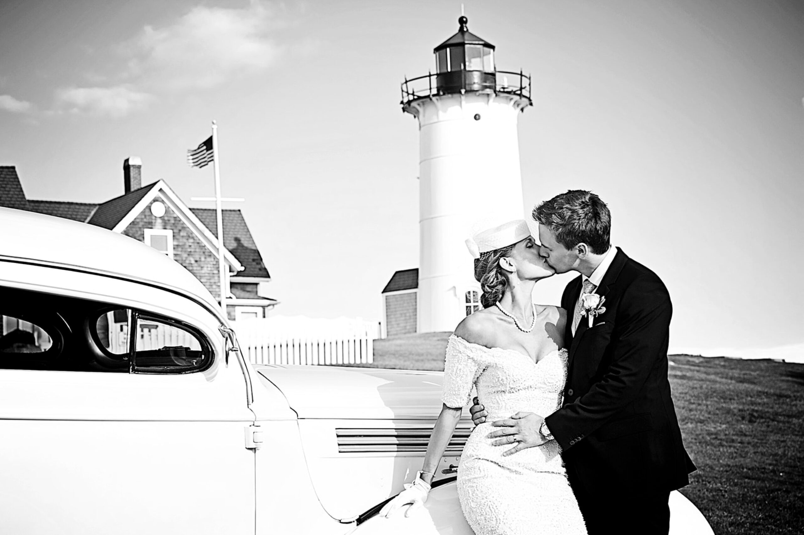Bride and Groom kiss in front of an antique car with Nobska Light House in the background