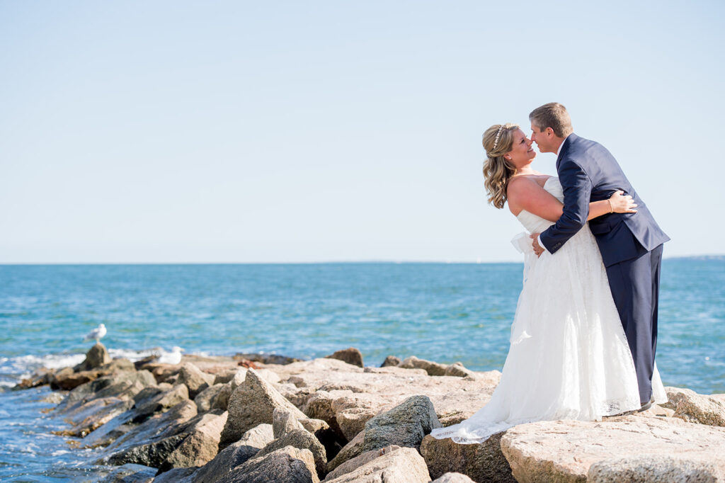 bride and groom about to kiss on a rock jetty with the ocean behind them for the wedding day