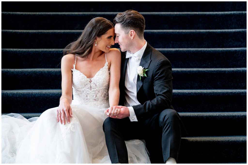 bride and groom sit on the stairs and smile at each other after their wedding