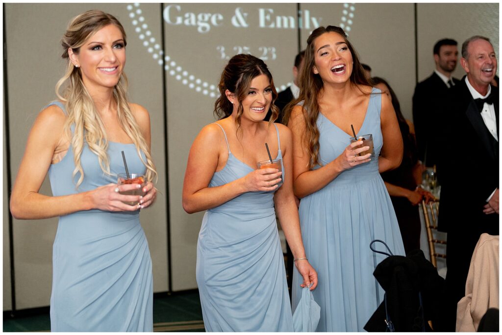 bridesmaid in light blue dresses laugh during the father's wedding toast