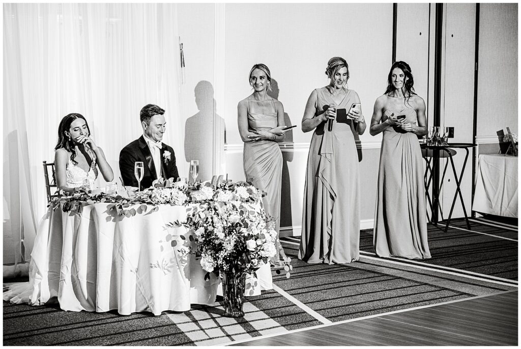 black and white photo of bride and groom laughing during the bridesmaids toast