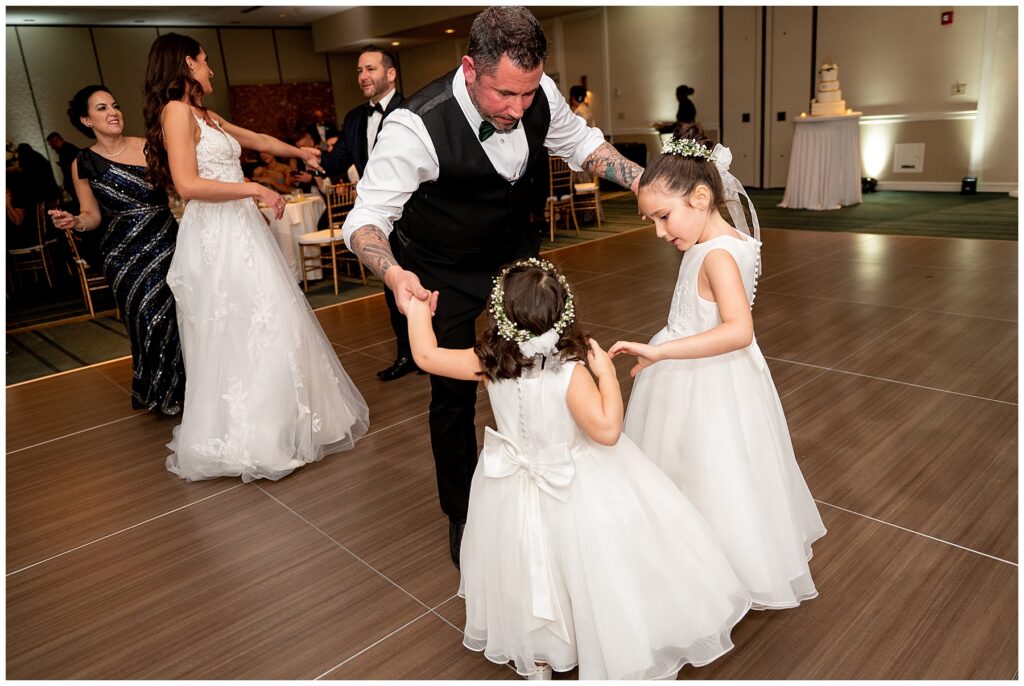 a father dances with the flower girls during the wedding reception