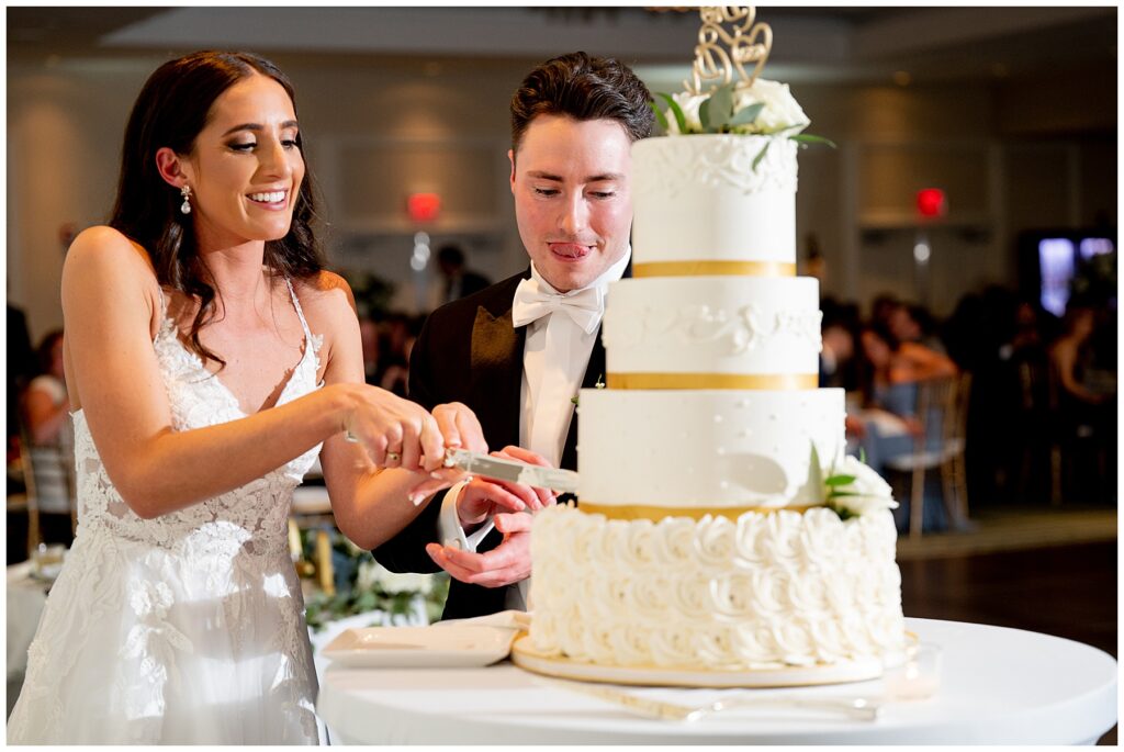 bride and groom begin to cut their white and gold wedding cake 