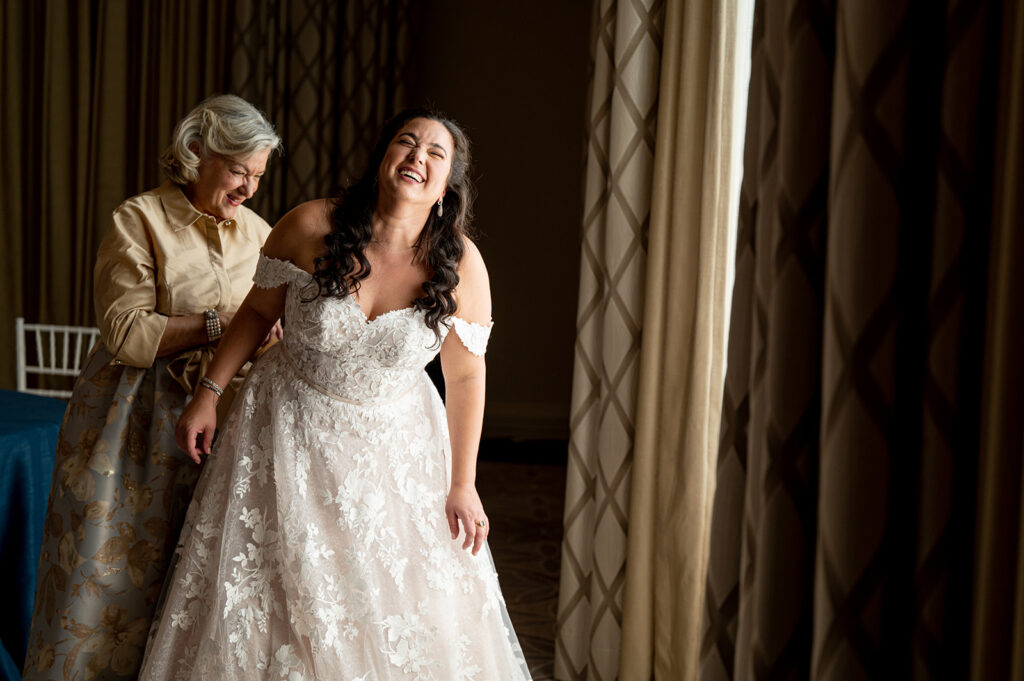 bride laughing as mother zips up her dress smiling 