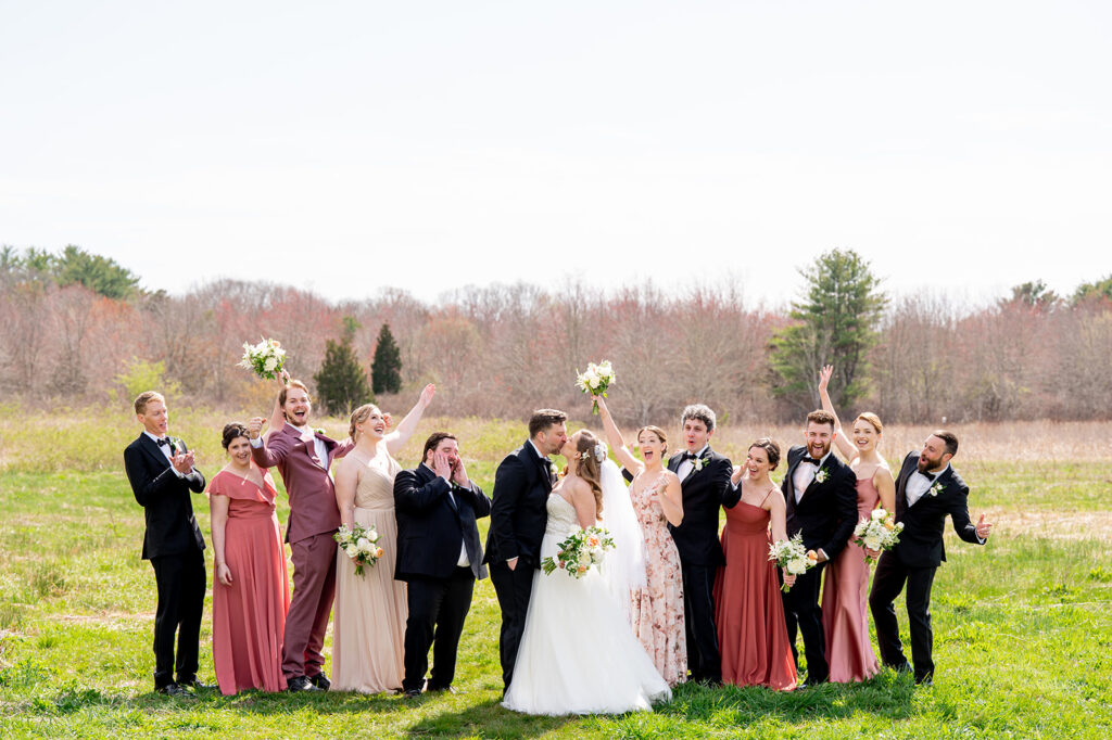 wedding party celebrating while bride and groom kiss