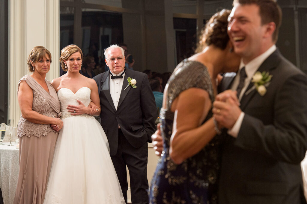 bride and her parents watch with tears in their eyes as groom dances with mom