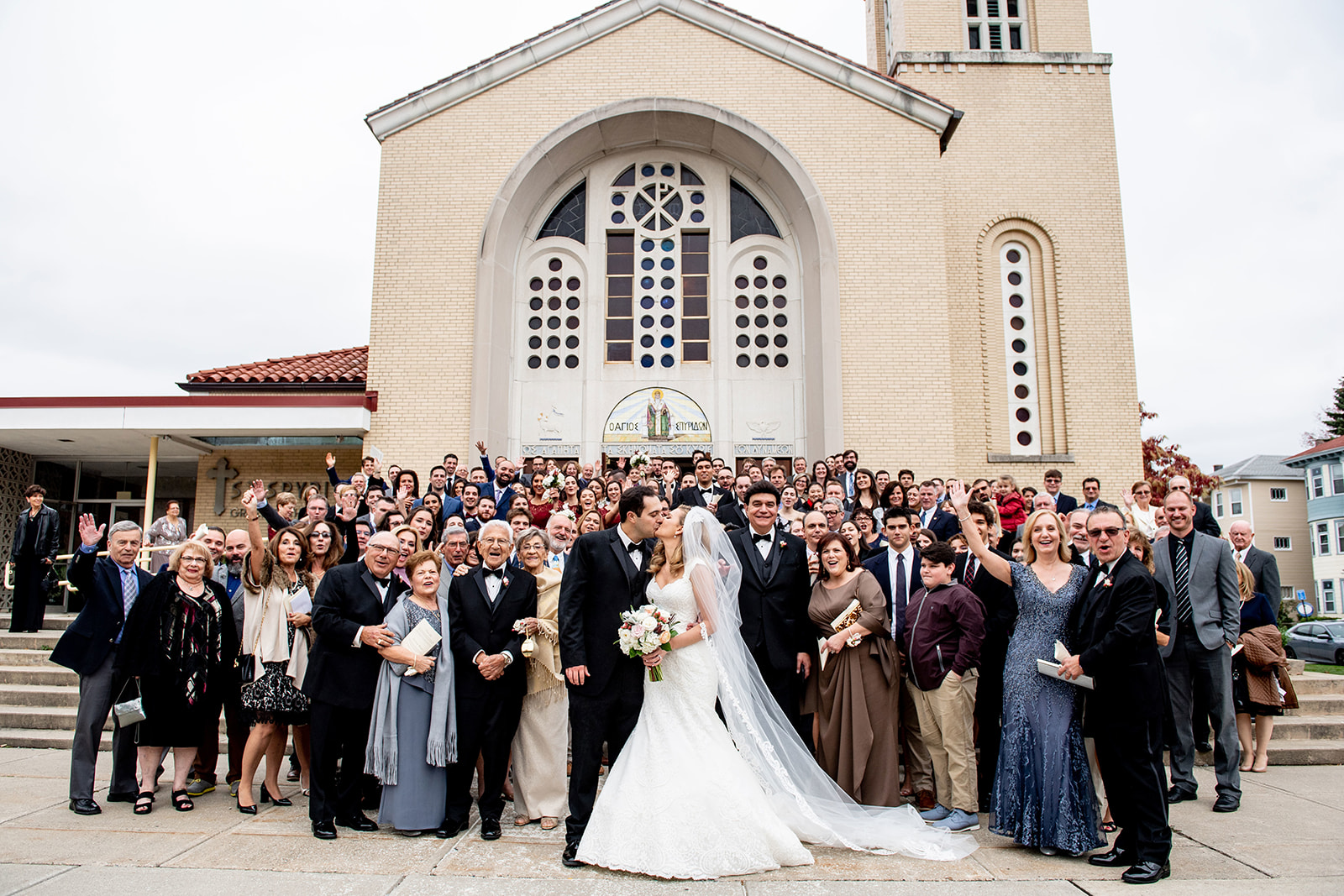 extended family photo with bride and groom in middle kissing in front of church