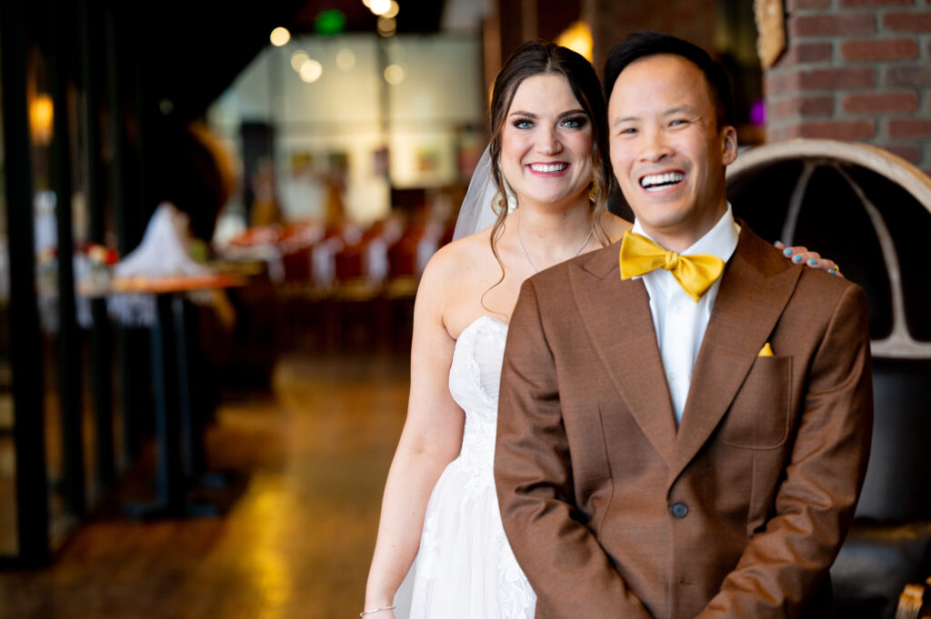 bride stands behind groom in brown suit just before he turns to see her for the first look 