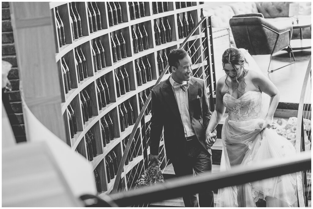 black and white photo of bride and groom walking down the stairs smiling 