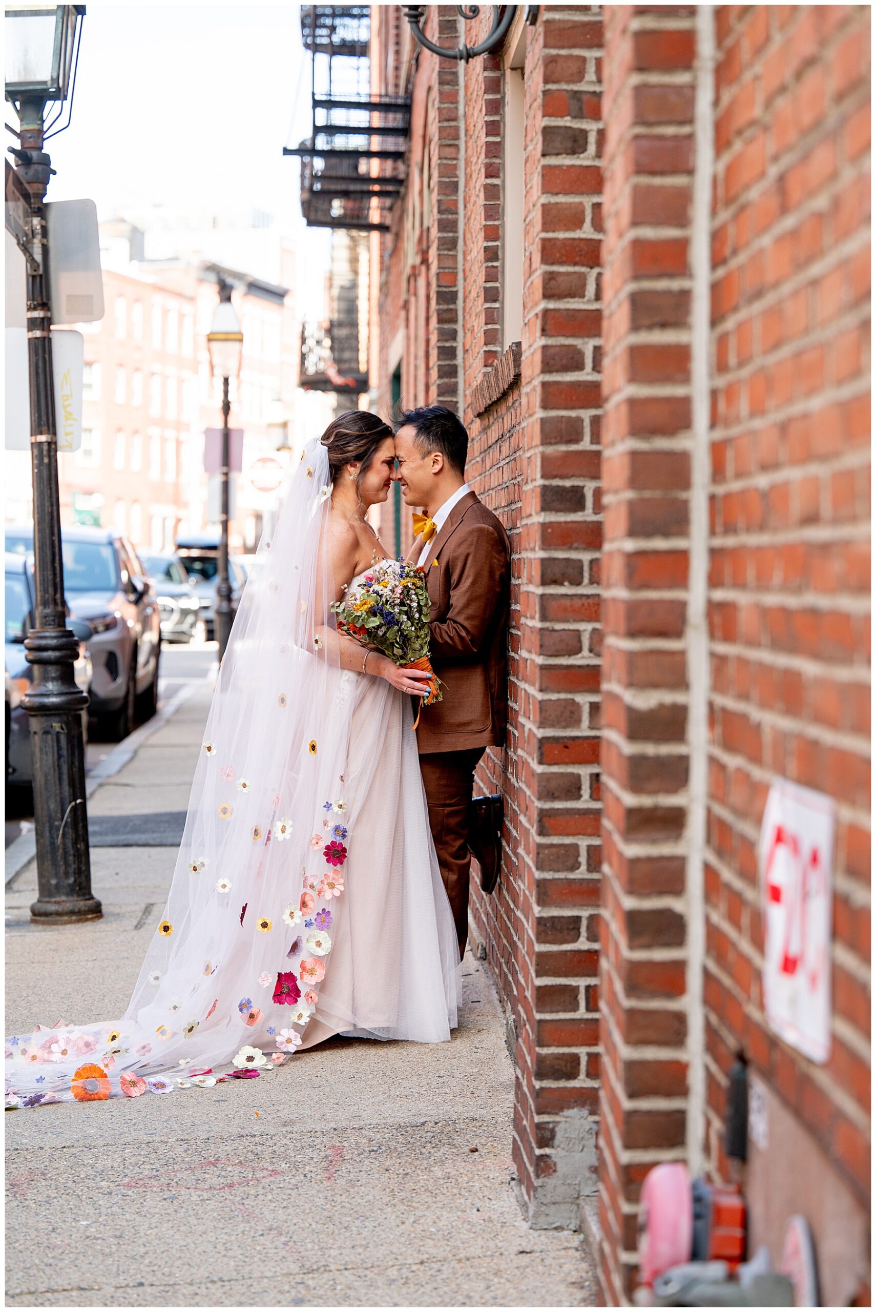 bride and groom lean against brick wall smiling