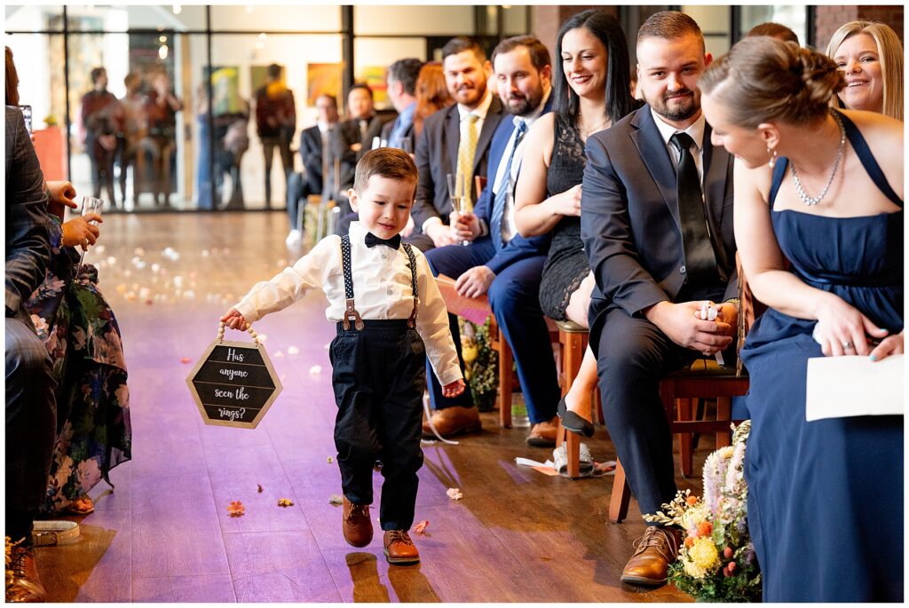 ring bearer walks down the aisle holding a sign that says has anyone seen the rings?