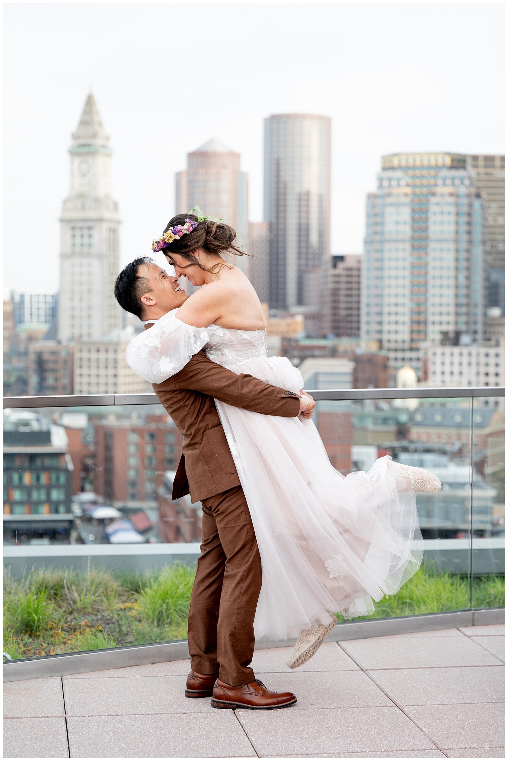 bride and groom embrace on the rooftop with the Boston skyline behind them