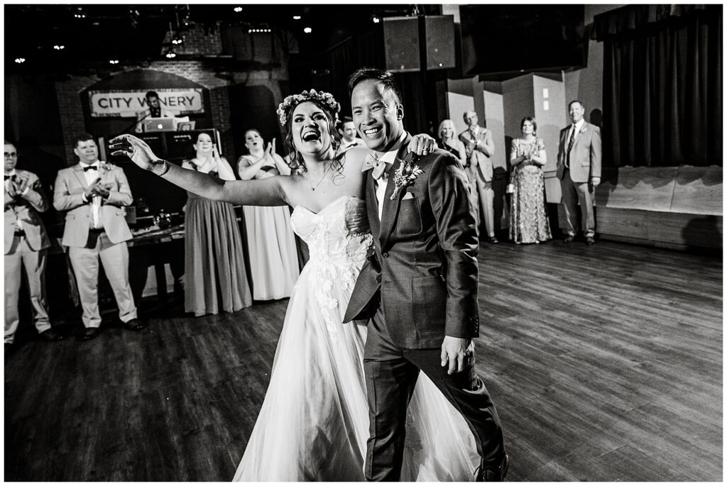 black and white photo of bride and groom smiling at guests at wedding reception