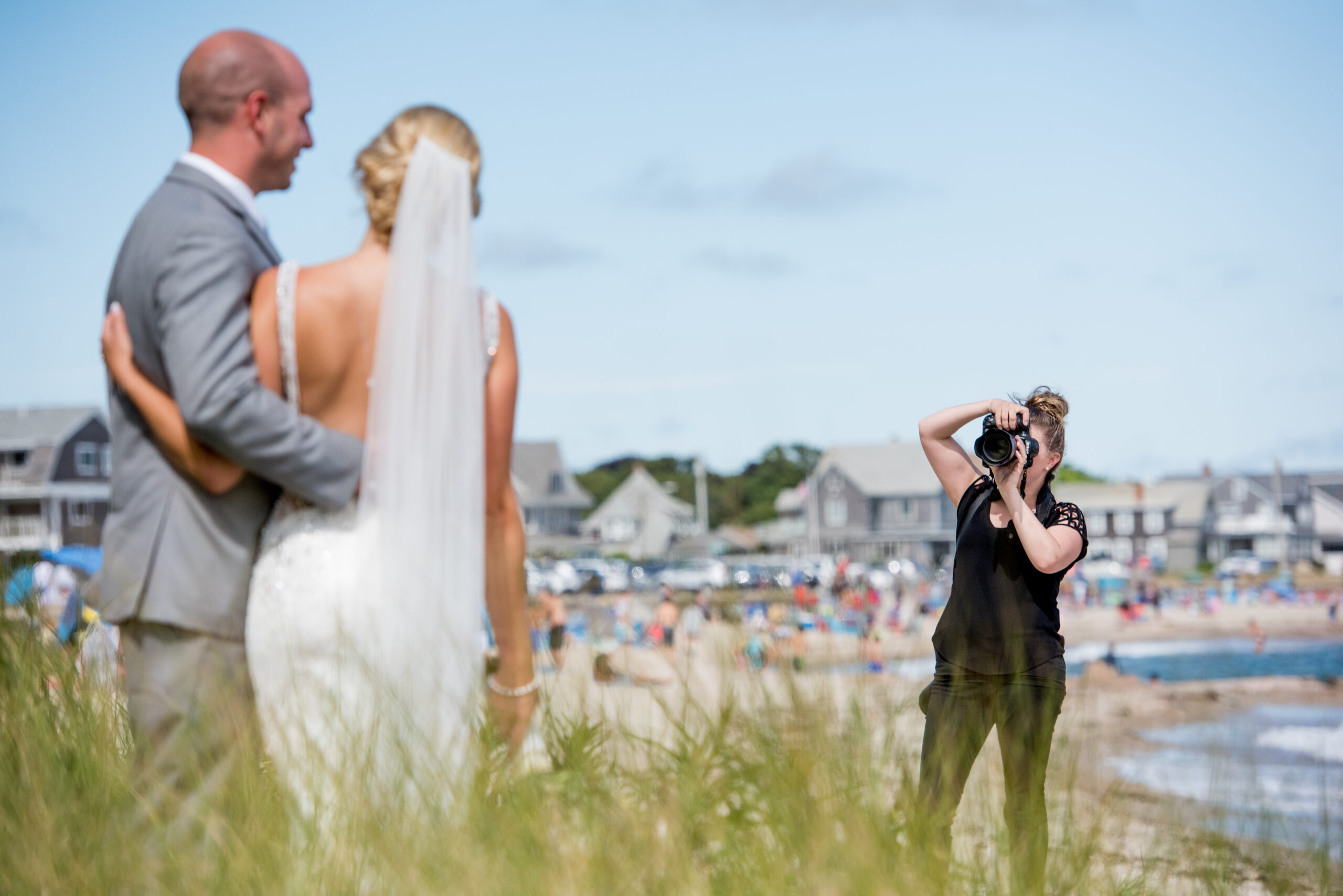 bride and groom face second shooter at wedding with crowded beach in background