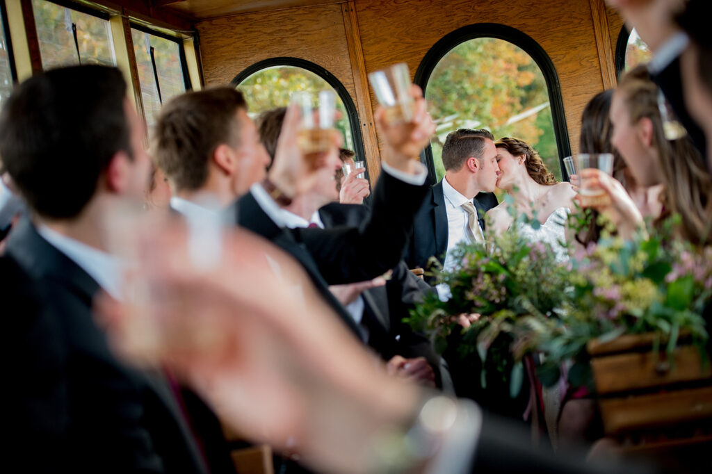 bride and groom kiss in the back of a trolley as wedding party raises glasses to cheers