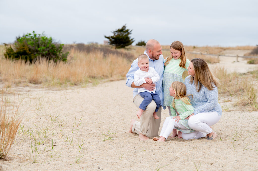 a family with two daughters and a younger son sit together on the beach smiling