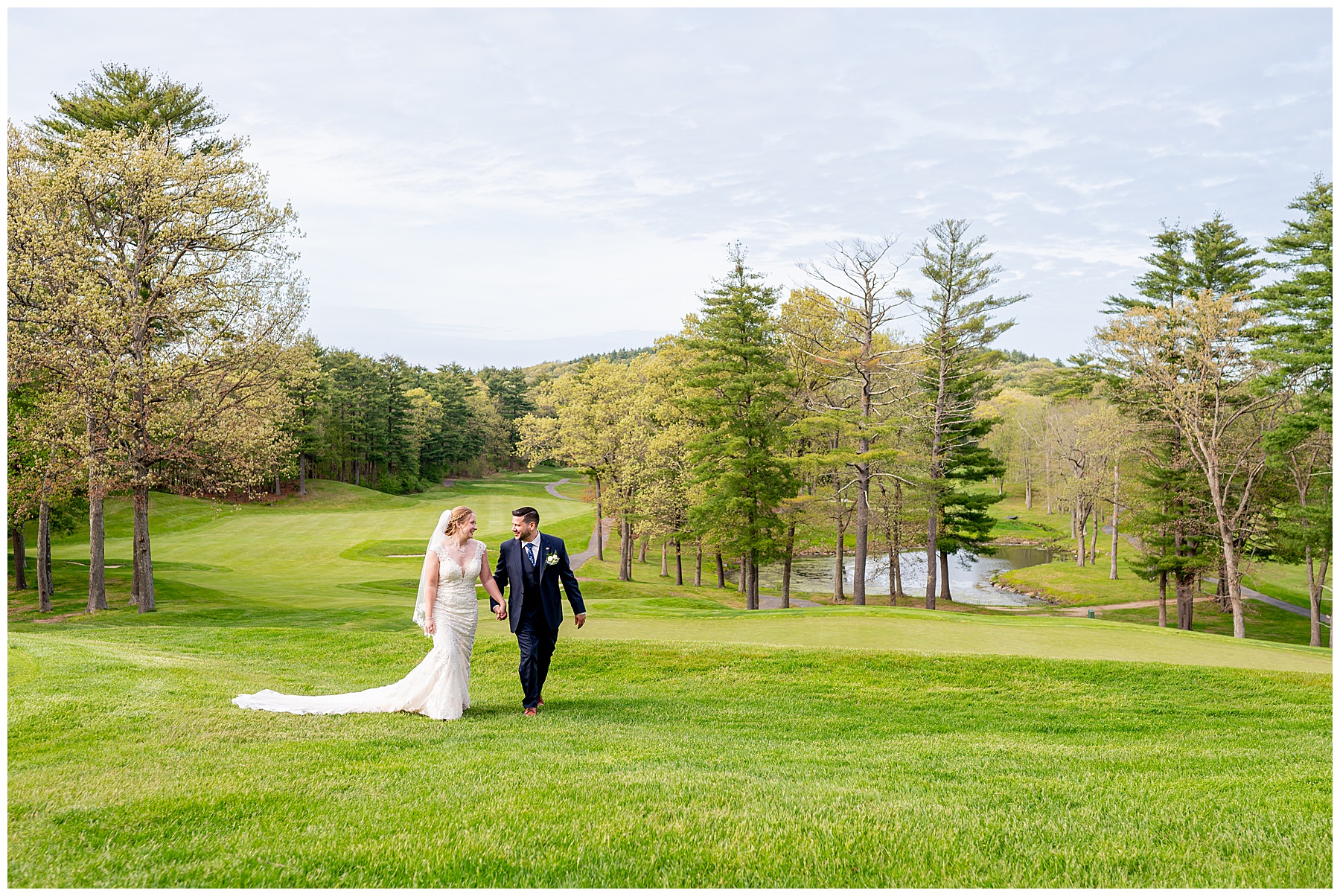 bride and groom holding hands while walking up grass covered hill with blue sky behind them