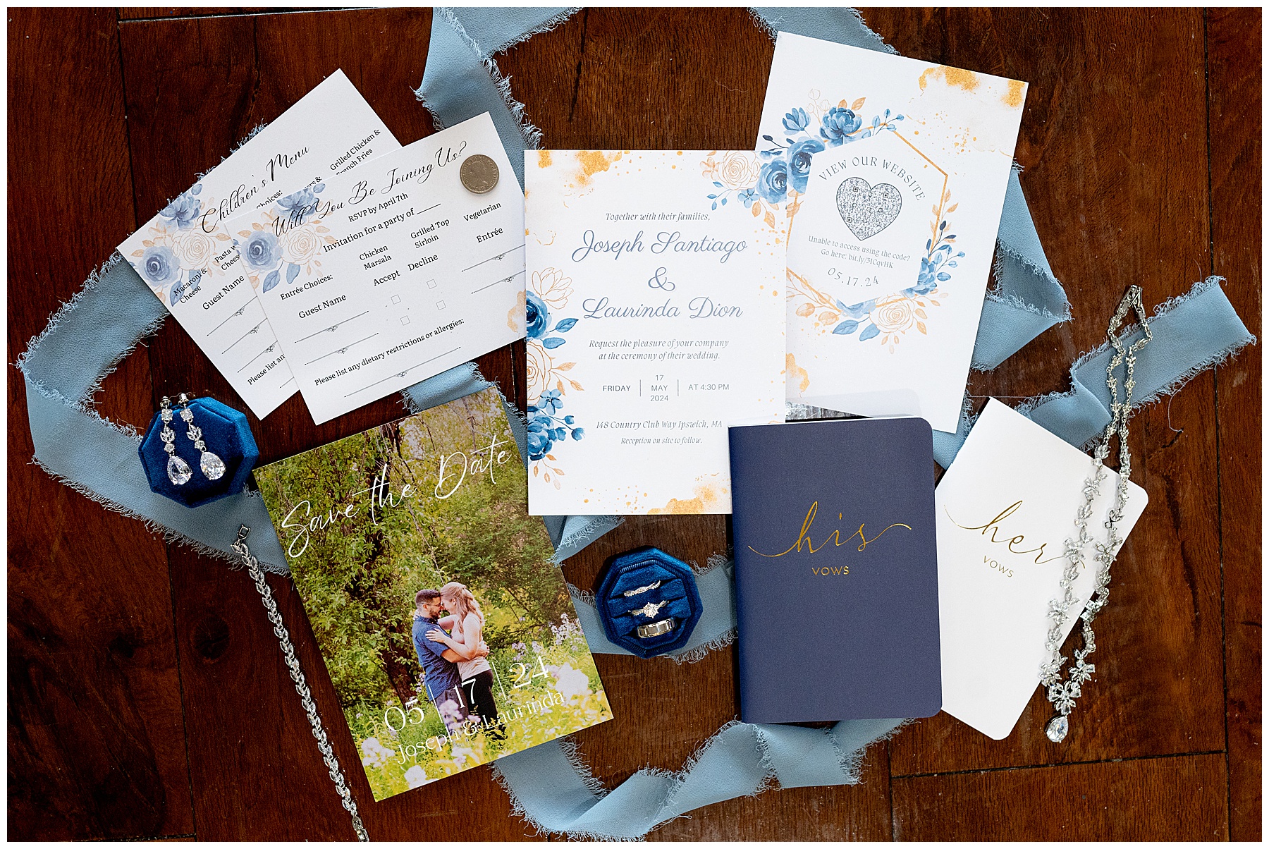 a flatlay of blue Massachusetts wedding invitation and vow books and bridal jewelry spread on a table 