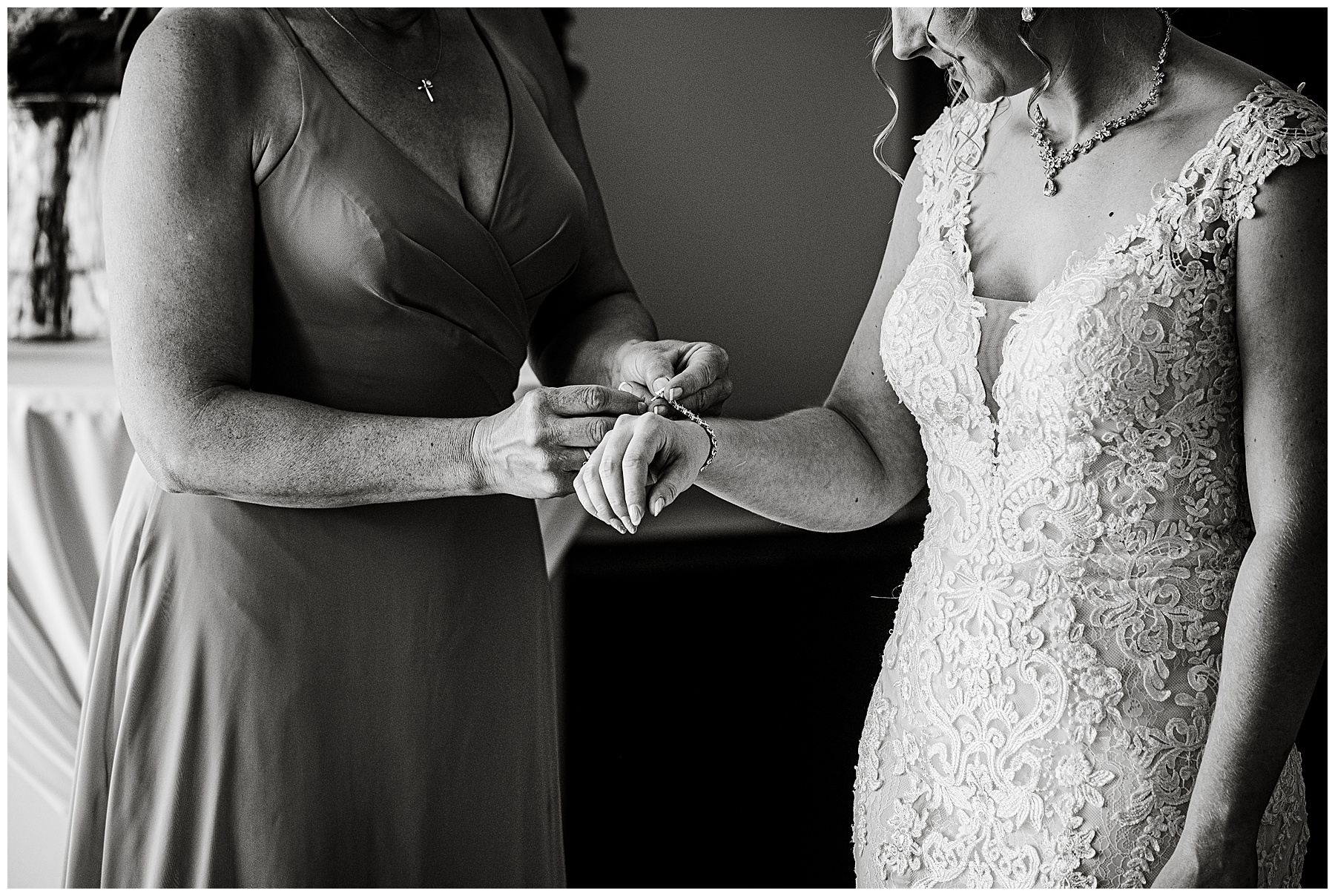 a black and white photo of a bridesmaid helping put a bracelet on the bride 