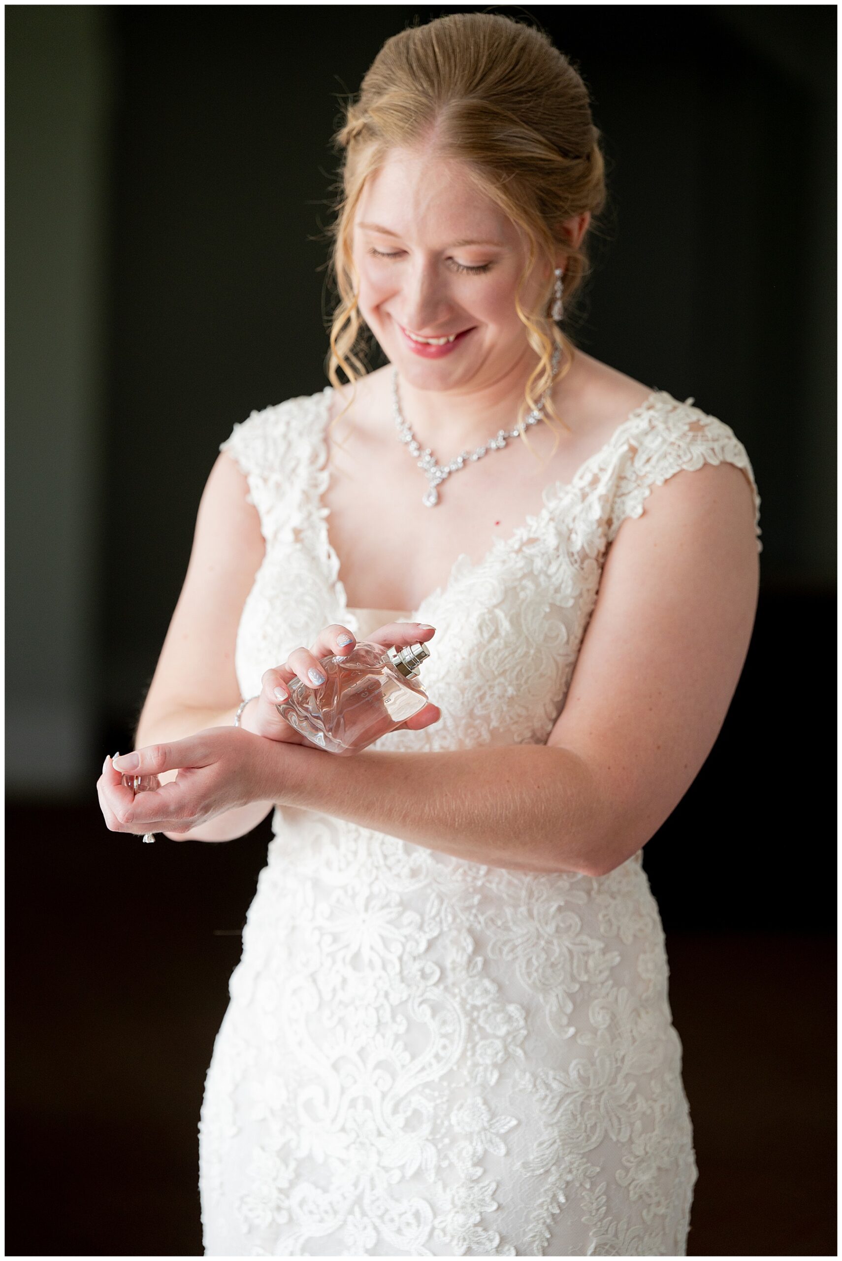 a bride smiles in her wedding dress as she puts on perfume