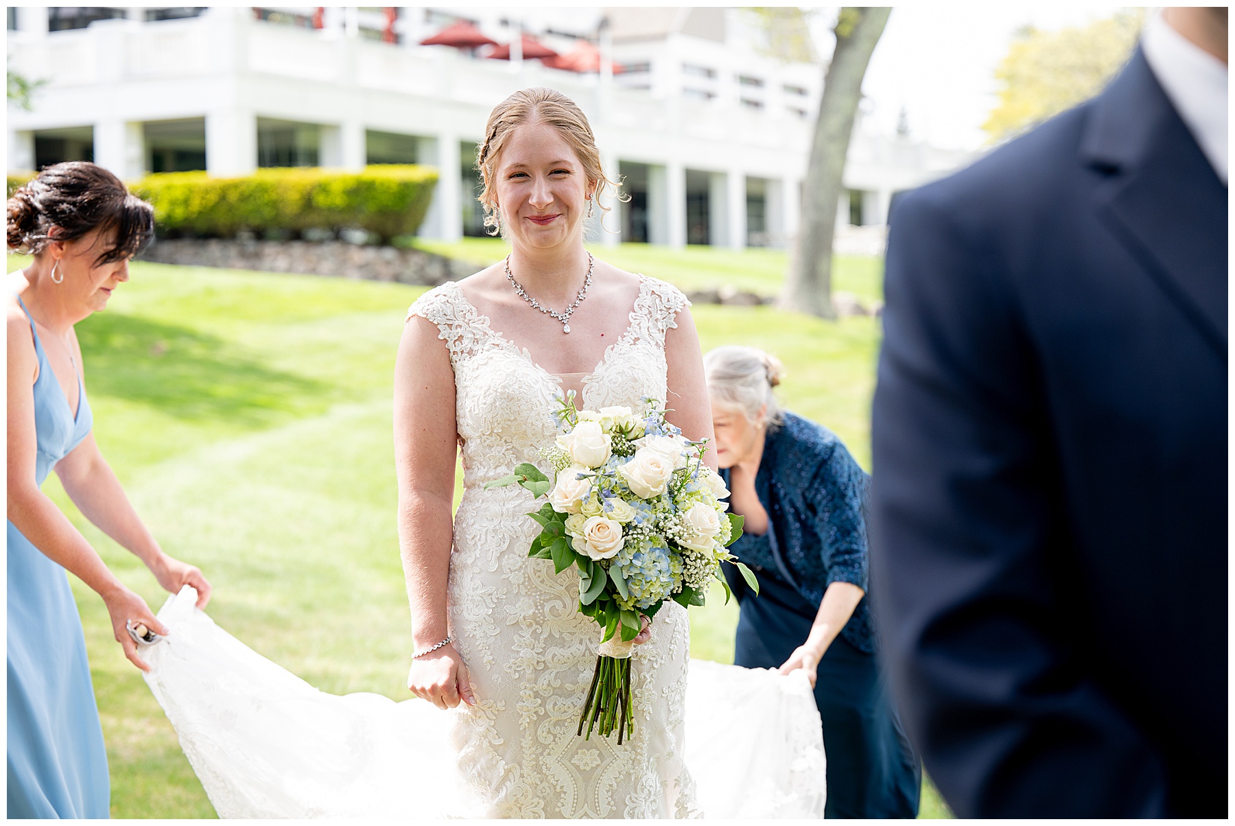 the bride smiles behind the groom holding a white flower bouquet