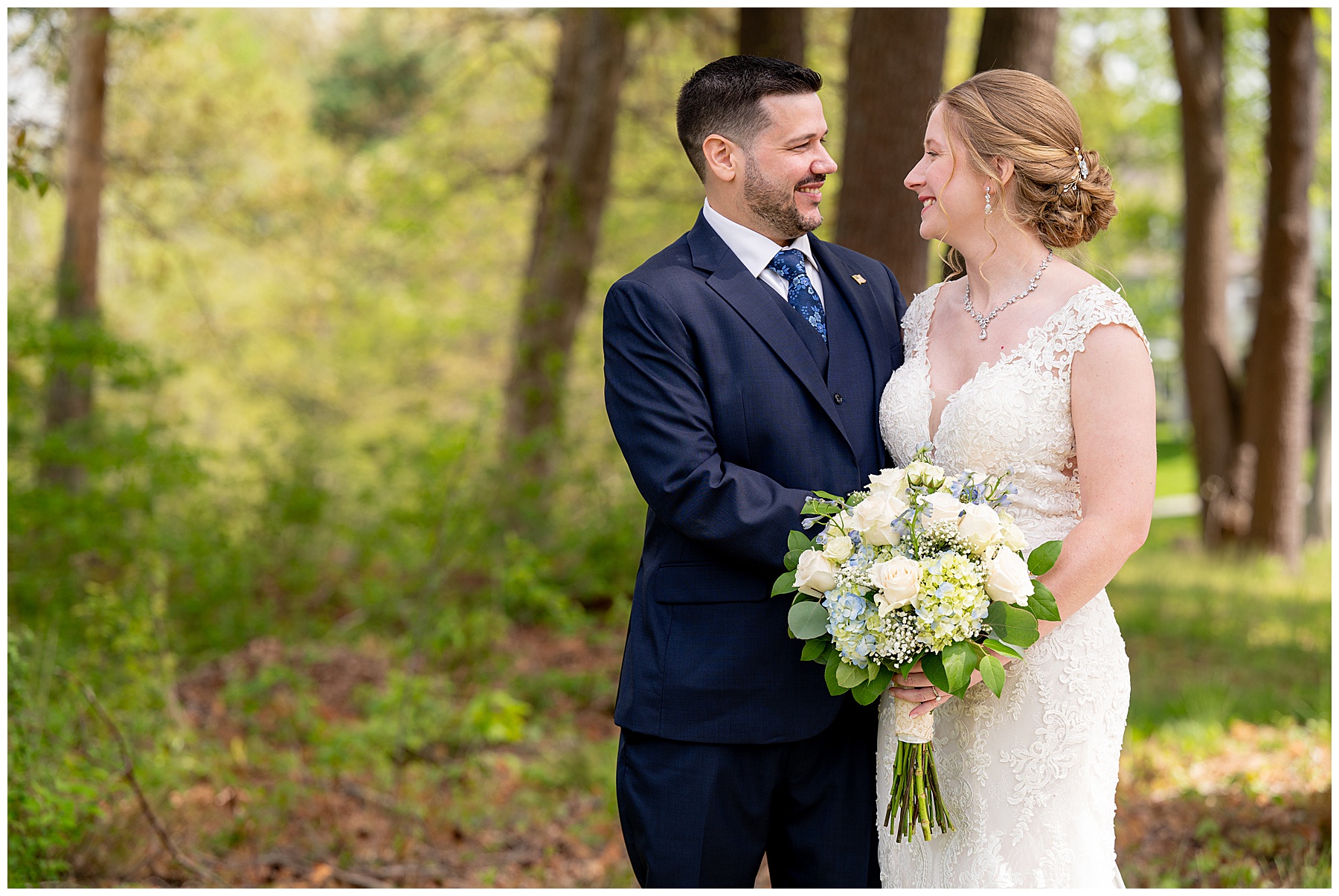 the bride holding her bouquet and groom in a navy suit smile at each other 