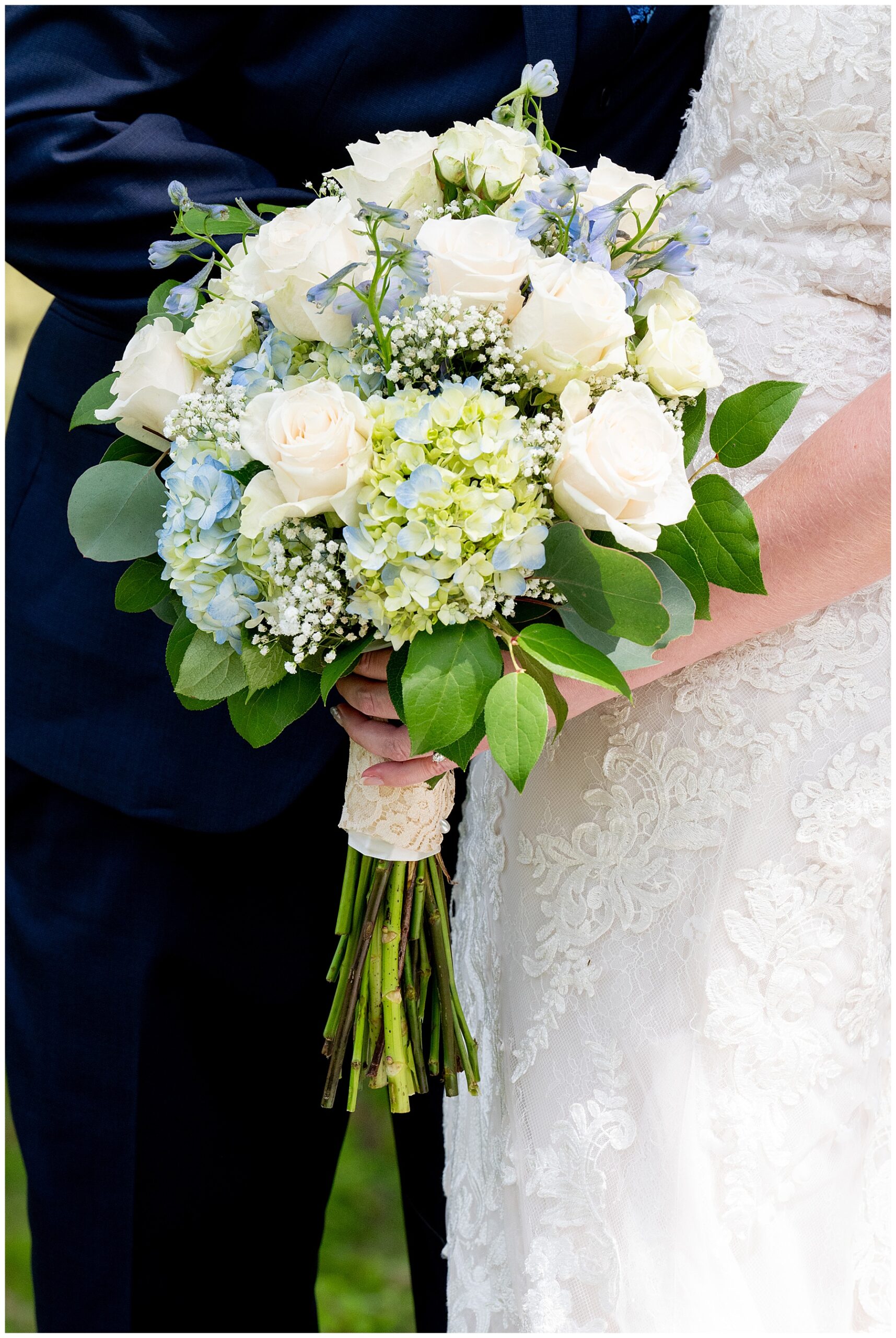 Detail photo of a bridal bouquet full of white and blue flowers and green leaves with long stems by Pinard's Florist based in Ayer, MA