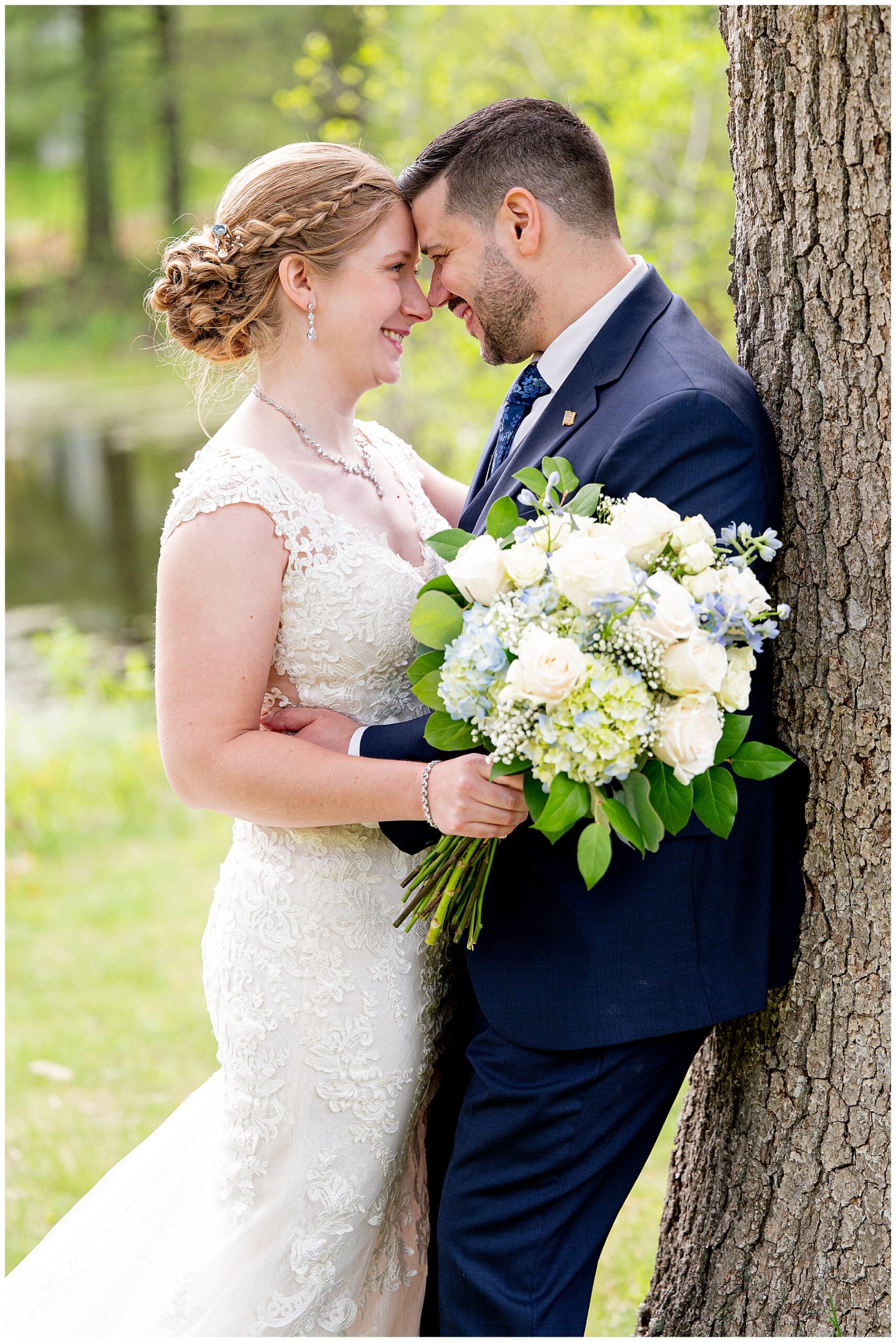 bride and groom touch forwards and smile as they lean against a tree 