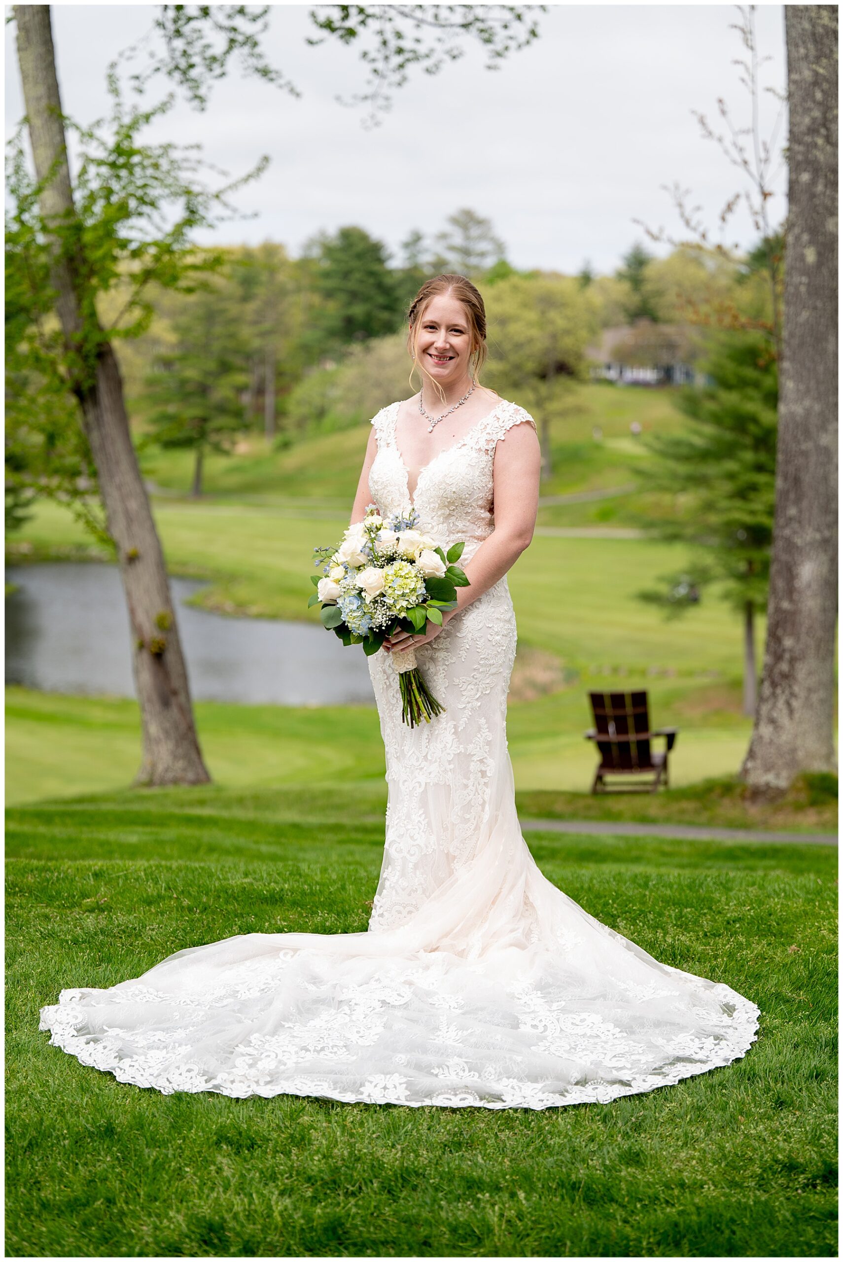 the bride stands in front of the grassy area holding her bouquet with her lace wedding dress and train 