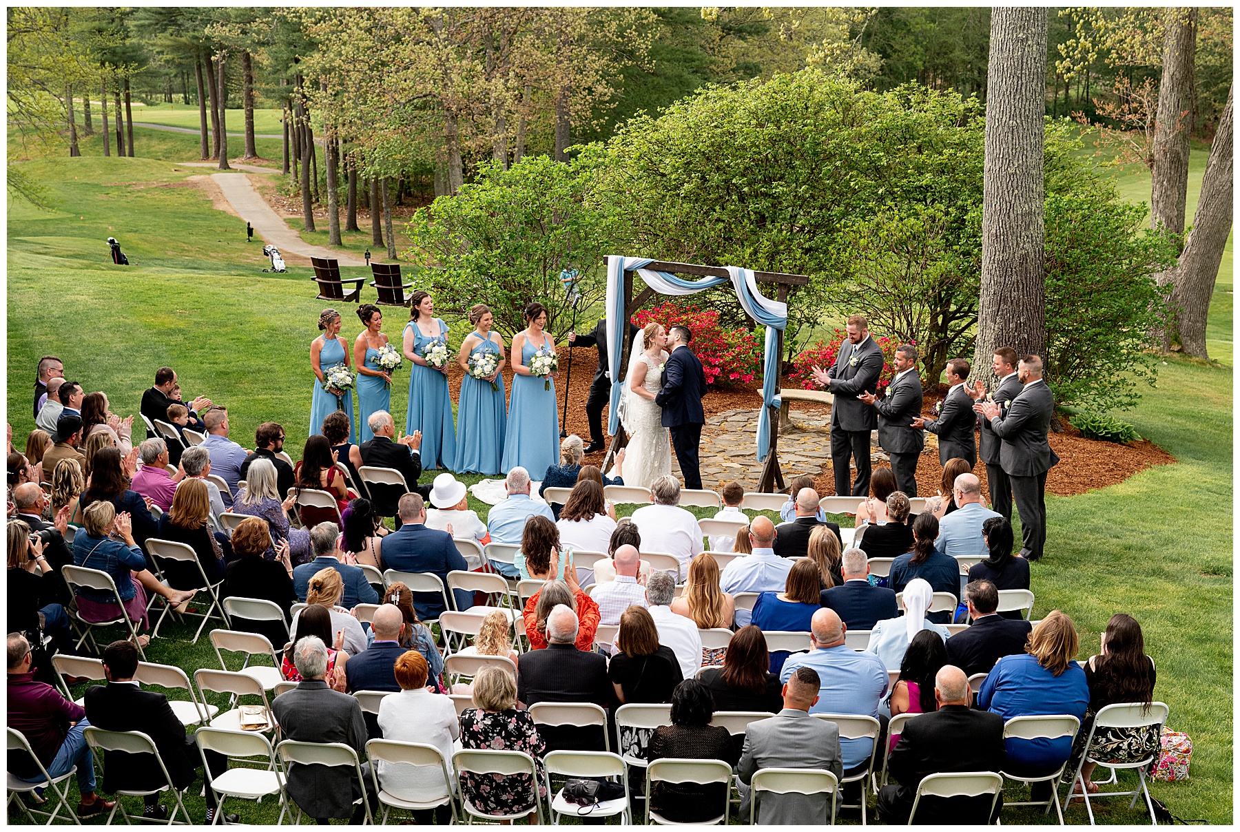 the bride and groom kiss at the end of the wedding ceremony surrounded by their guests