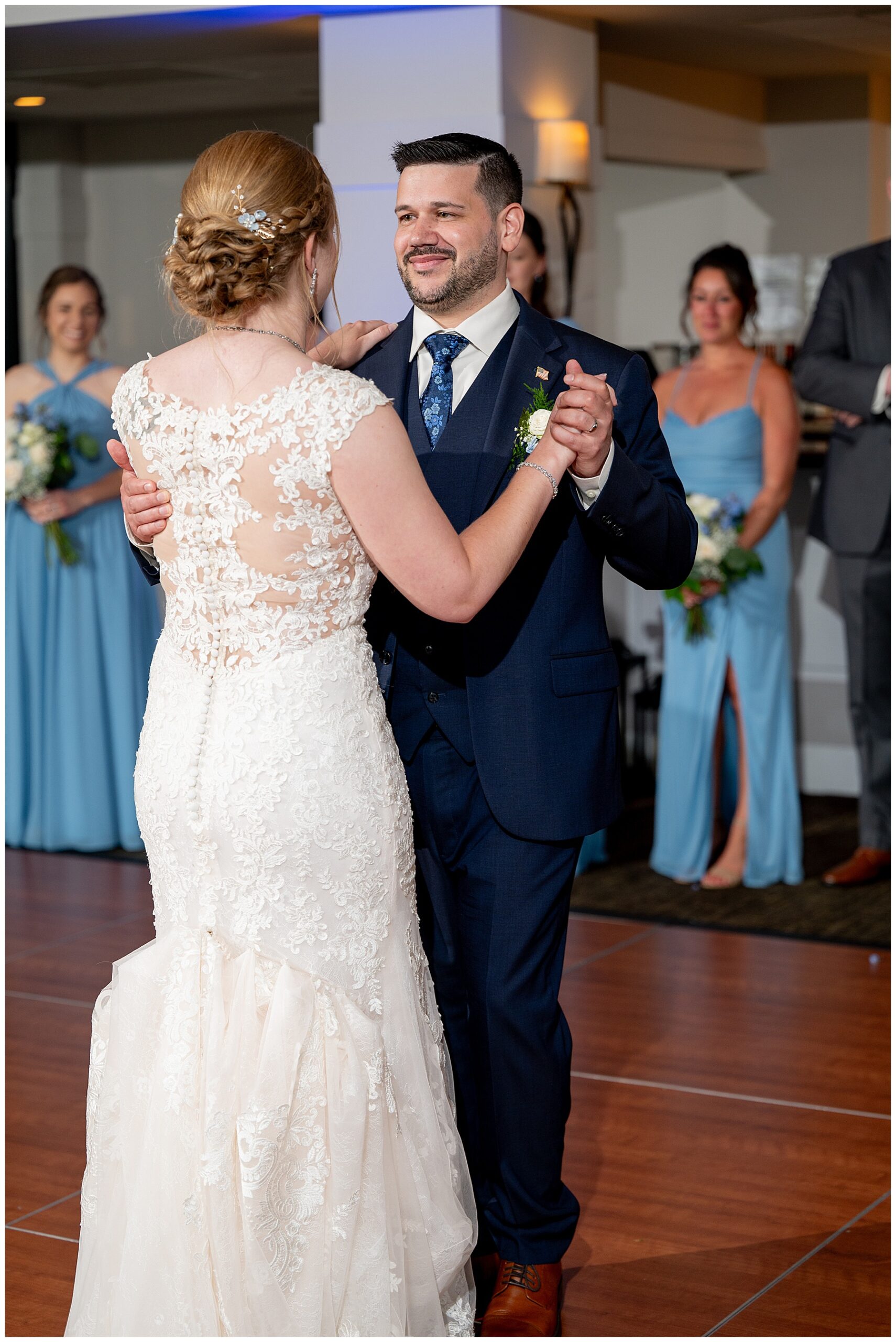 a photo of the bride & groom during their first dance as wedding party looks on 