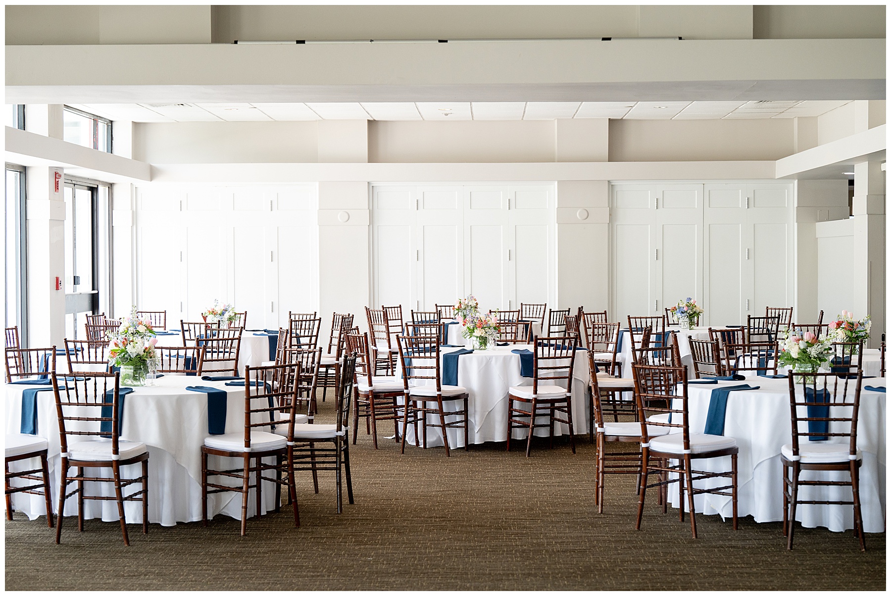 a photo of the reception space at Ipswich Country Club a Massachusetts wedding venue with white table cloths and blue napkins and white and green flower centerpieces 