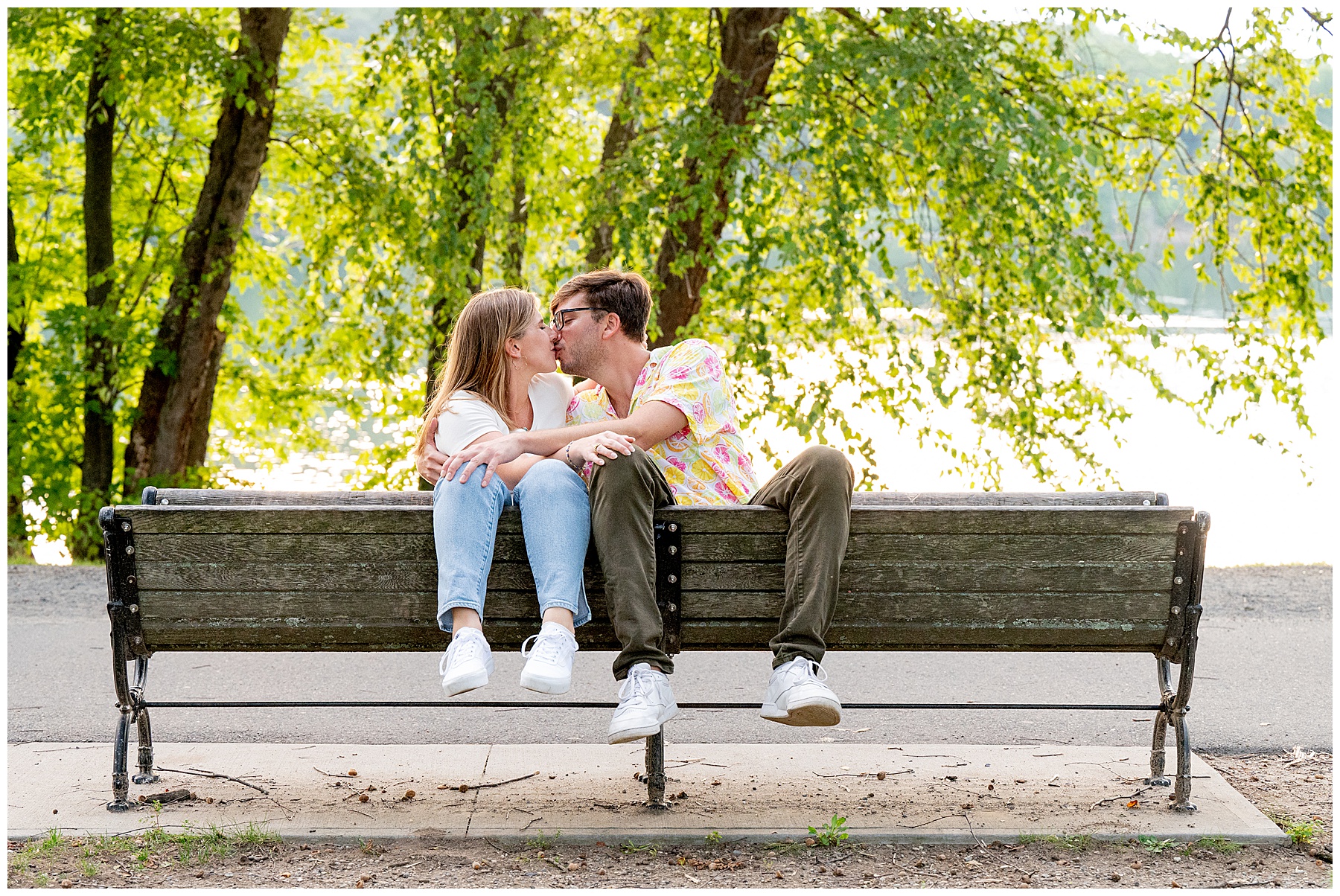 man and woman sitting on the back of a park bench at Jamaica Pond in boston kissing