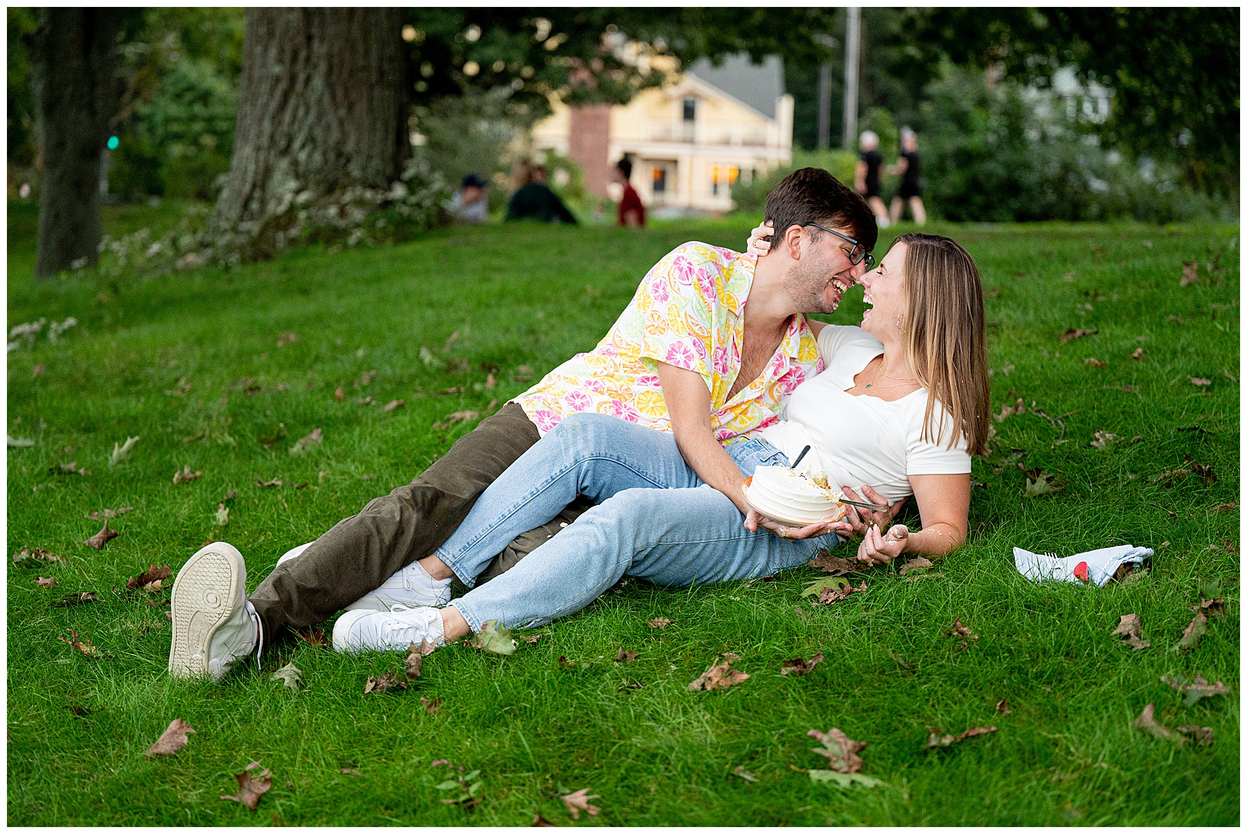 couple laughing and laying on grassy knoll during their boston engagement session 