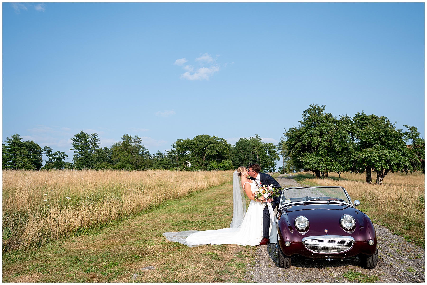 bride and groom kissing as they lean against a maroon antique car at their fruitlands museum wedding