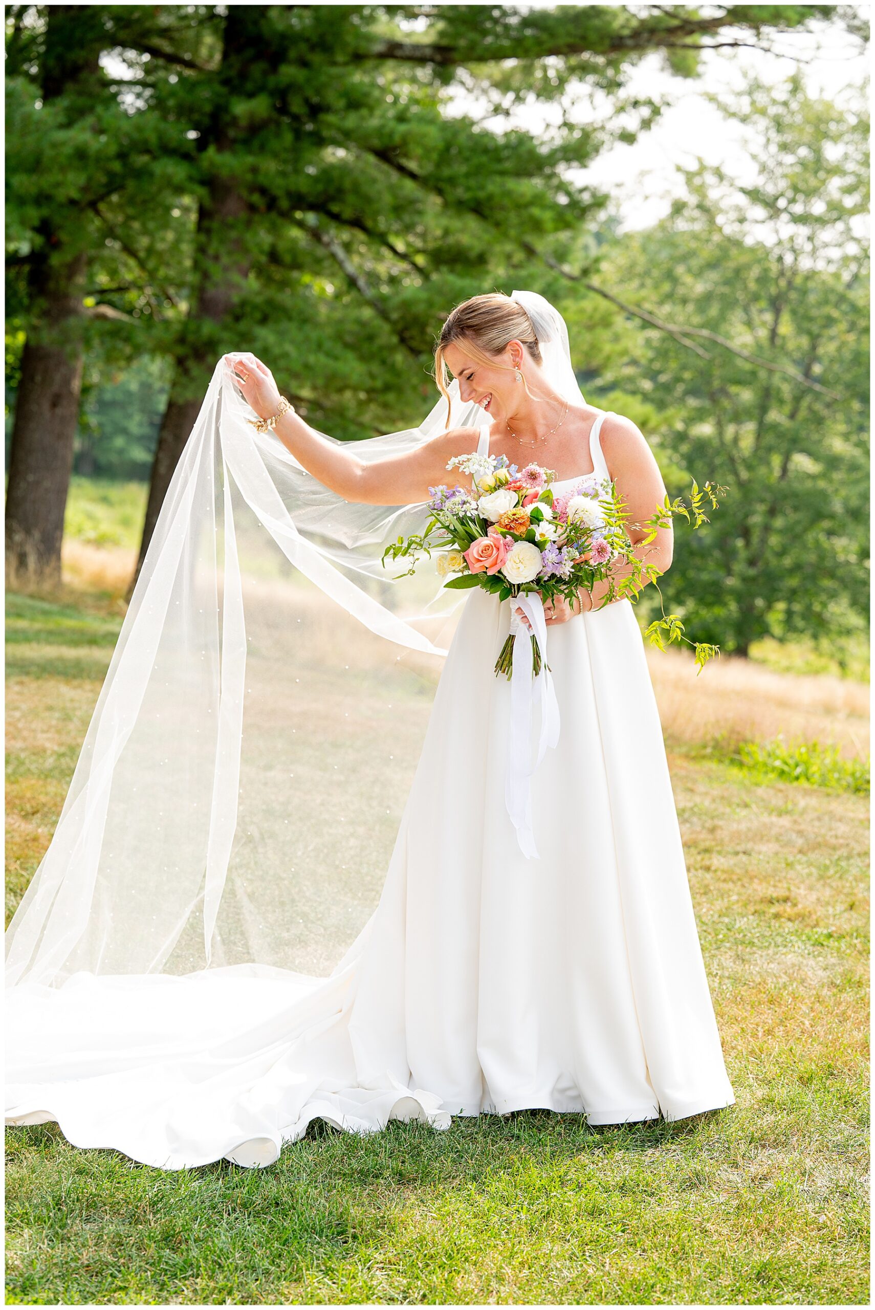 bride smiling and holding her veil and bouquet at her Fruitlands Museum Wedding 