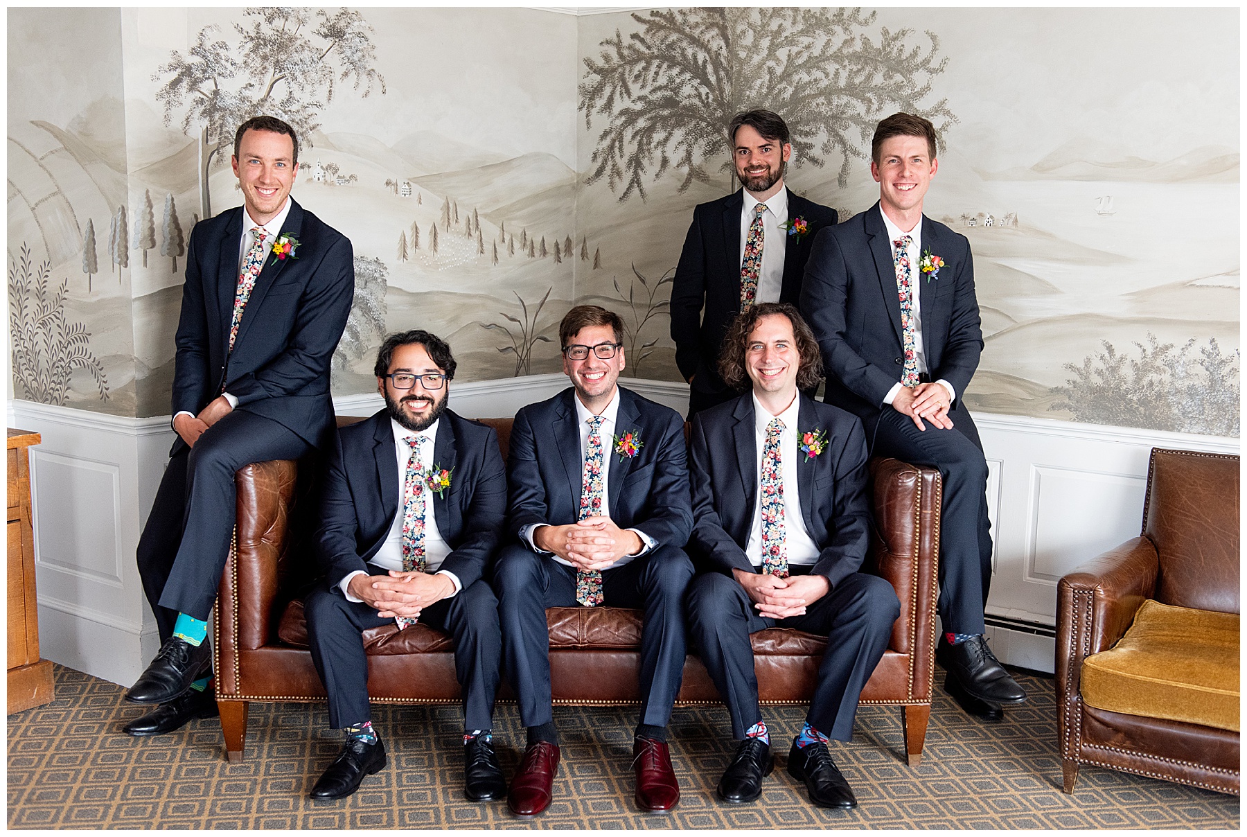 groom sitting down with groomsmen smiling at the camera all wearing a blue suits and floral patterned ties