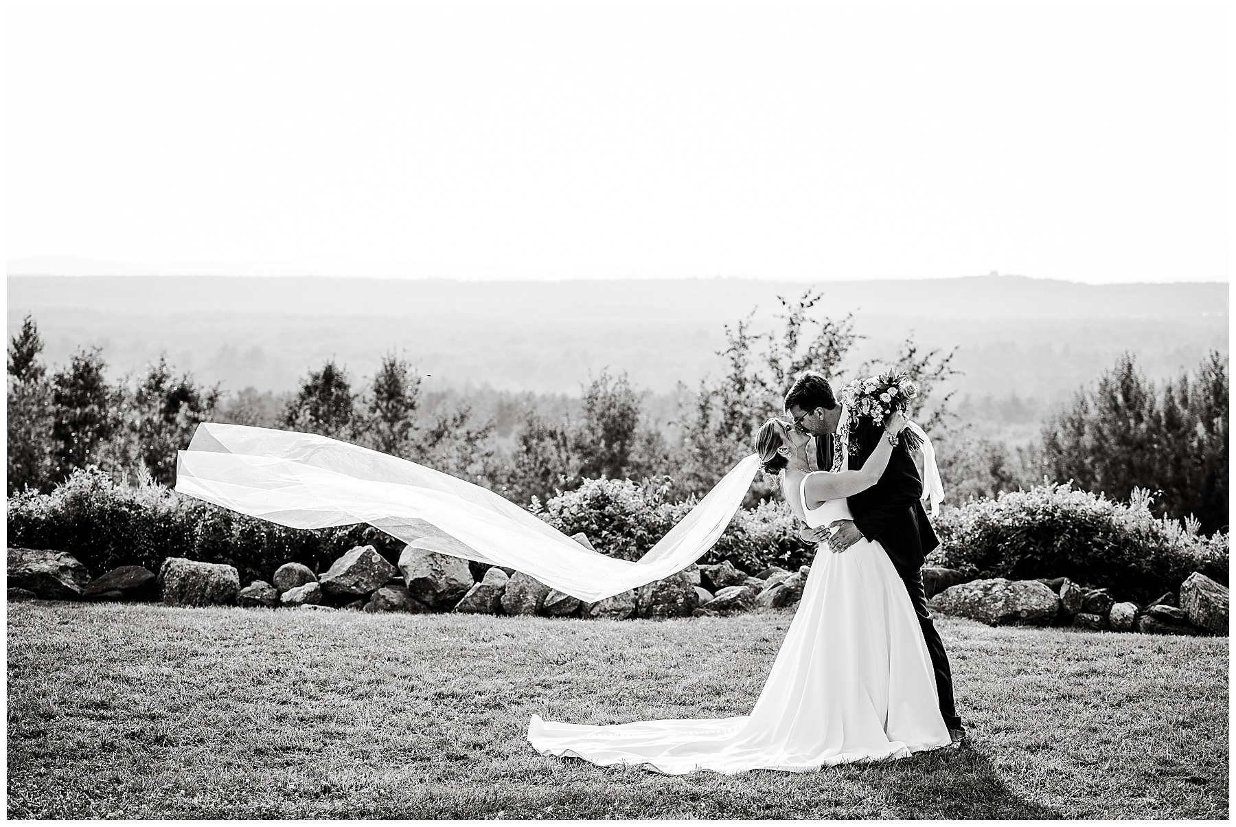 black and white photo of bride and groom kissing with her veil blowing in the breeze 