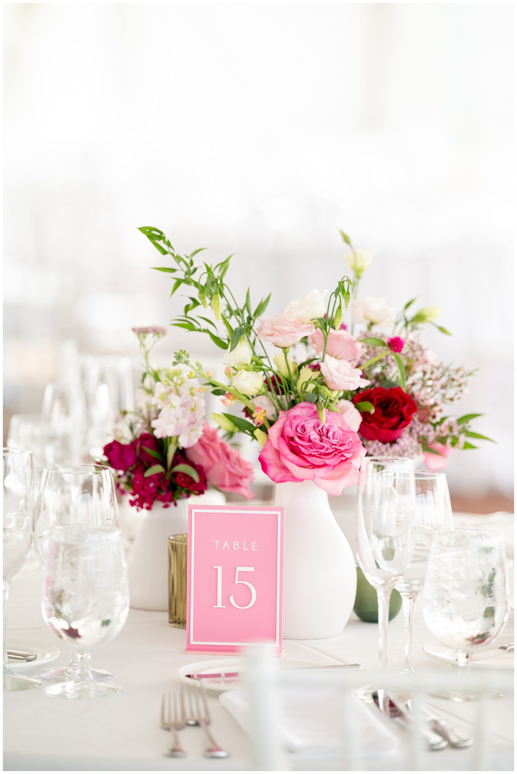 white vase filled with pink and red flowers and a pink table number at the wedding reception 