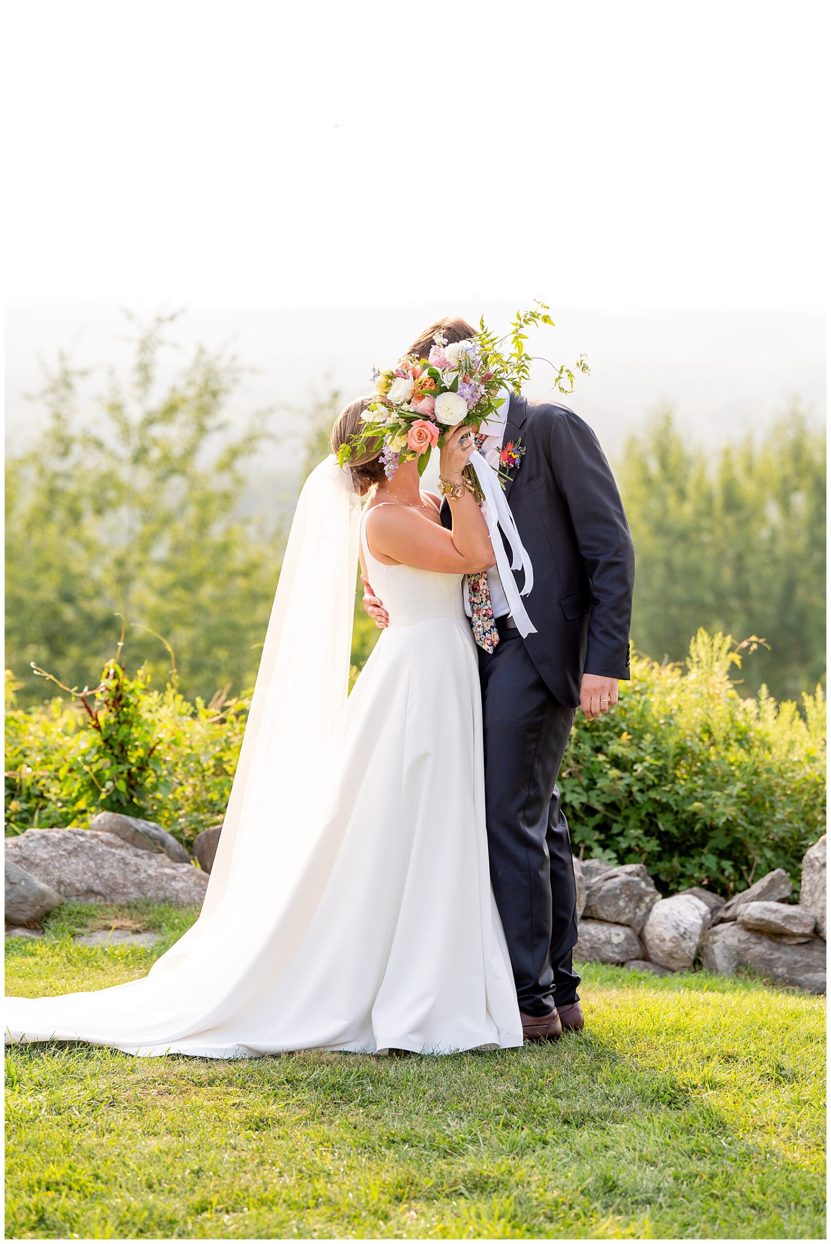 bride and groom kissing as bride holds up her floral bouquet 