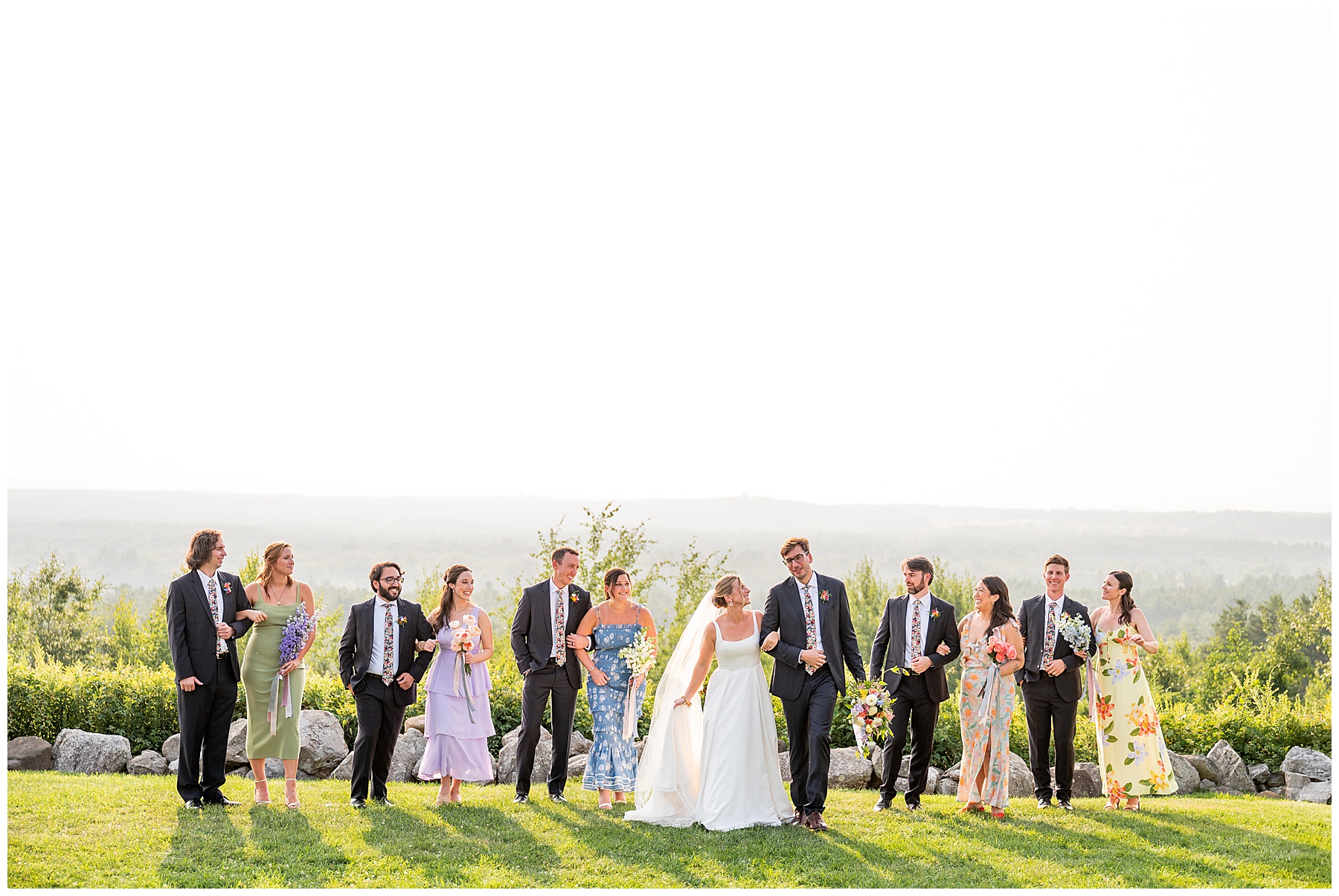 wedding party walking along the field at the Fruitlands Museum with bridesmaids in floral dresses and groomsmen in blue suits 