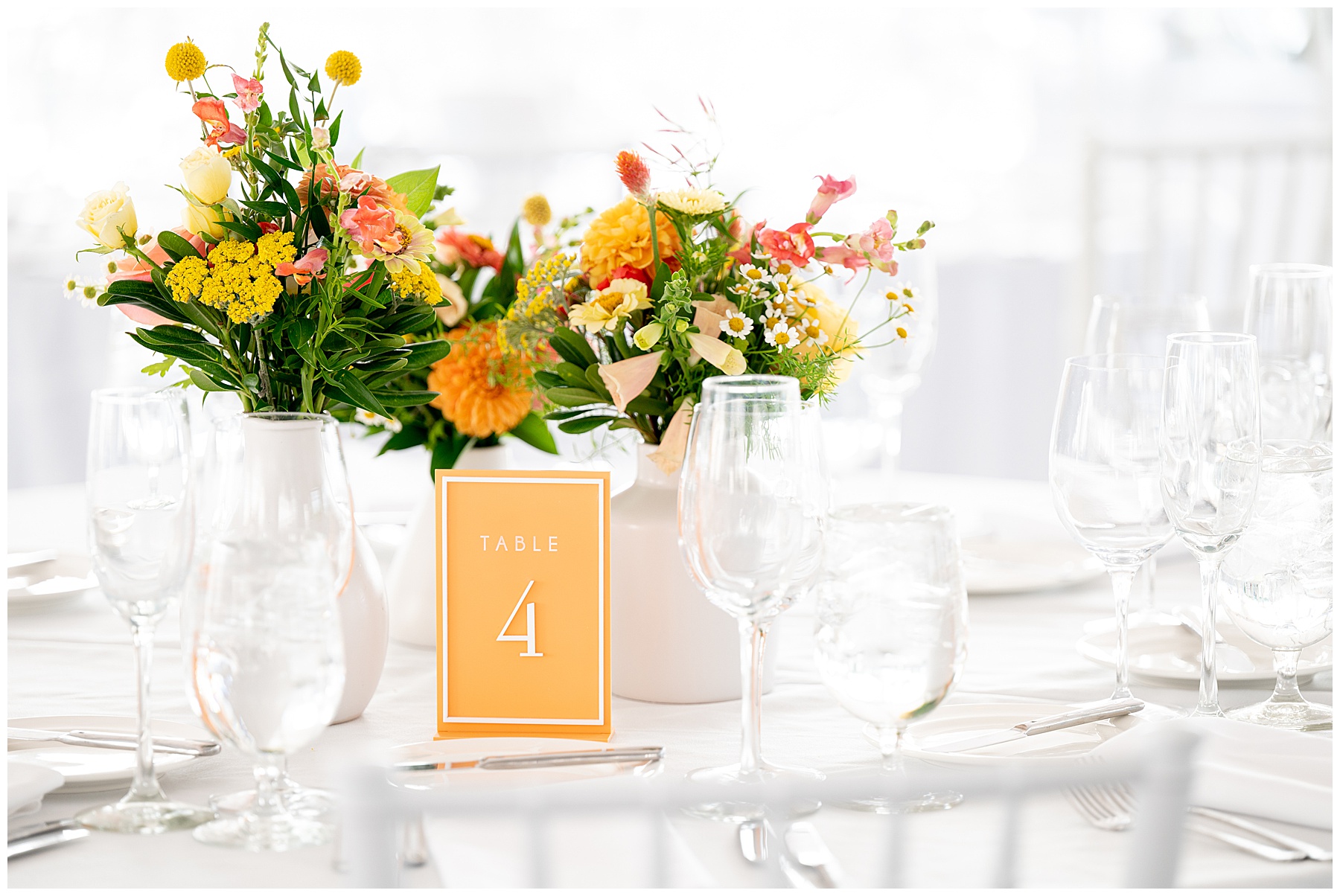 white vase filled with orange and yellow flowers and a orange table number at the wedding reception 