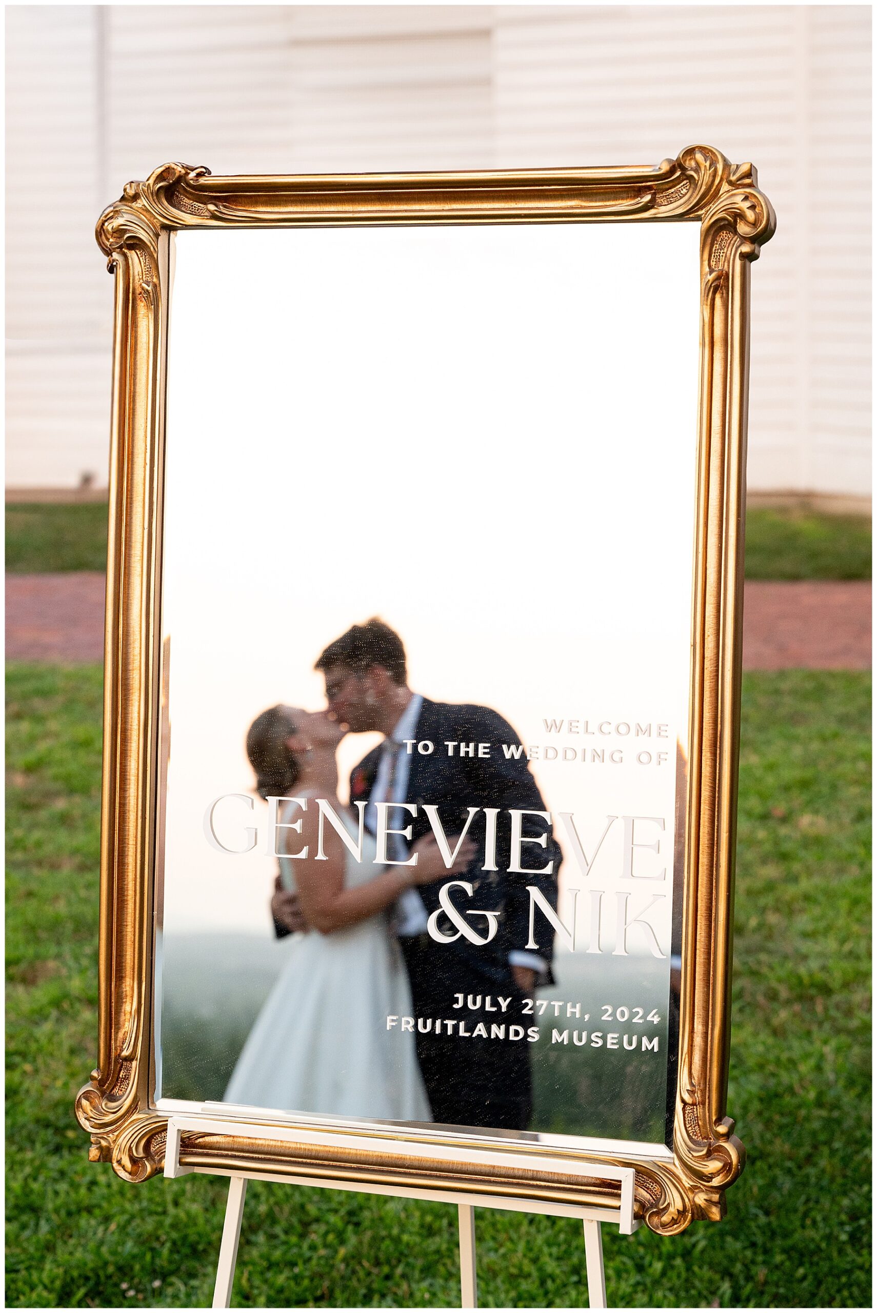 reflection of bride and groom kissing in mirror decor that reads welcome to the wedding at fruitlands museum 