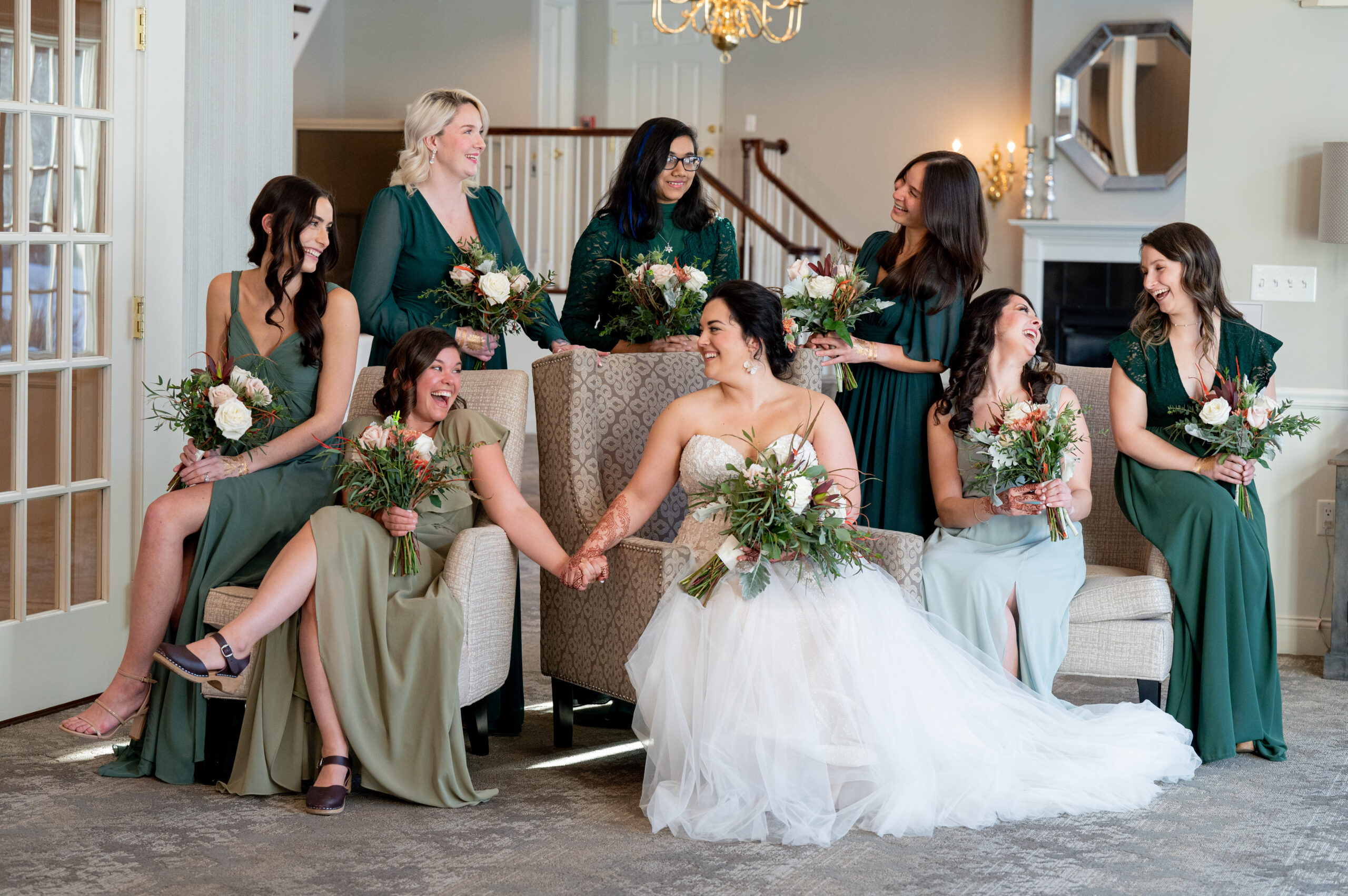 bride sitting with her bridesmaids who are wearing different shades of green 