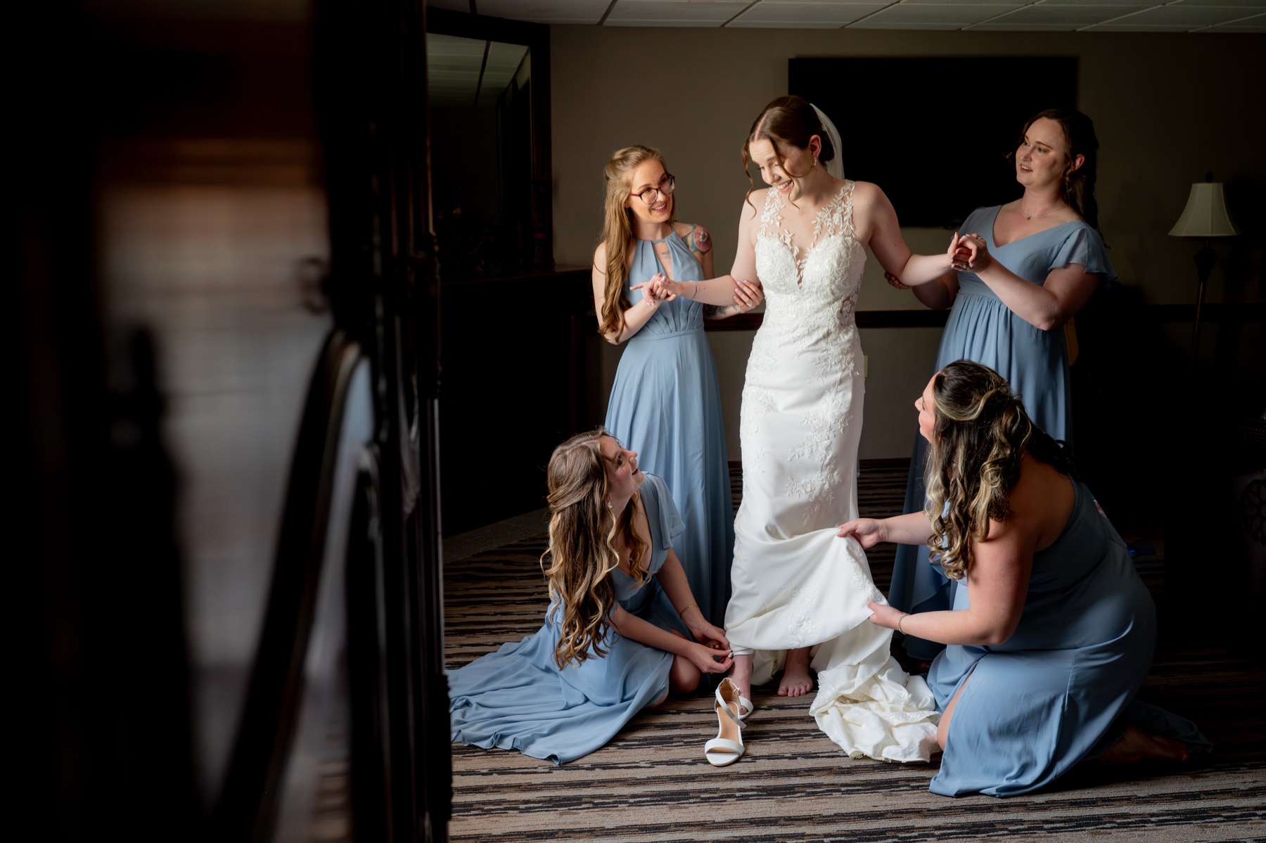 bride steps into her wedding shoes as bridesmaids wearing light blue dresses help her 