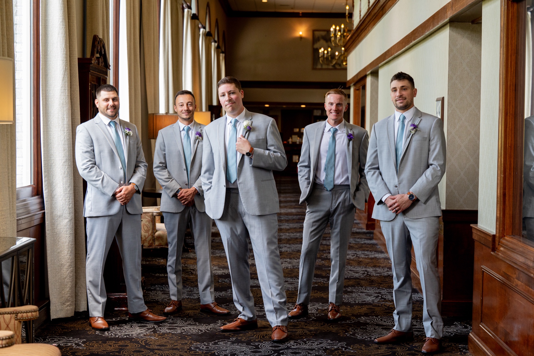 groom standing with his groomsmen all wearing light grey suits with blue ties 