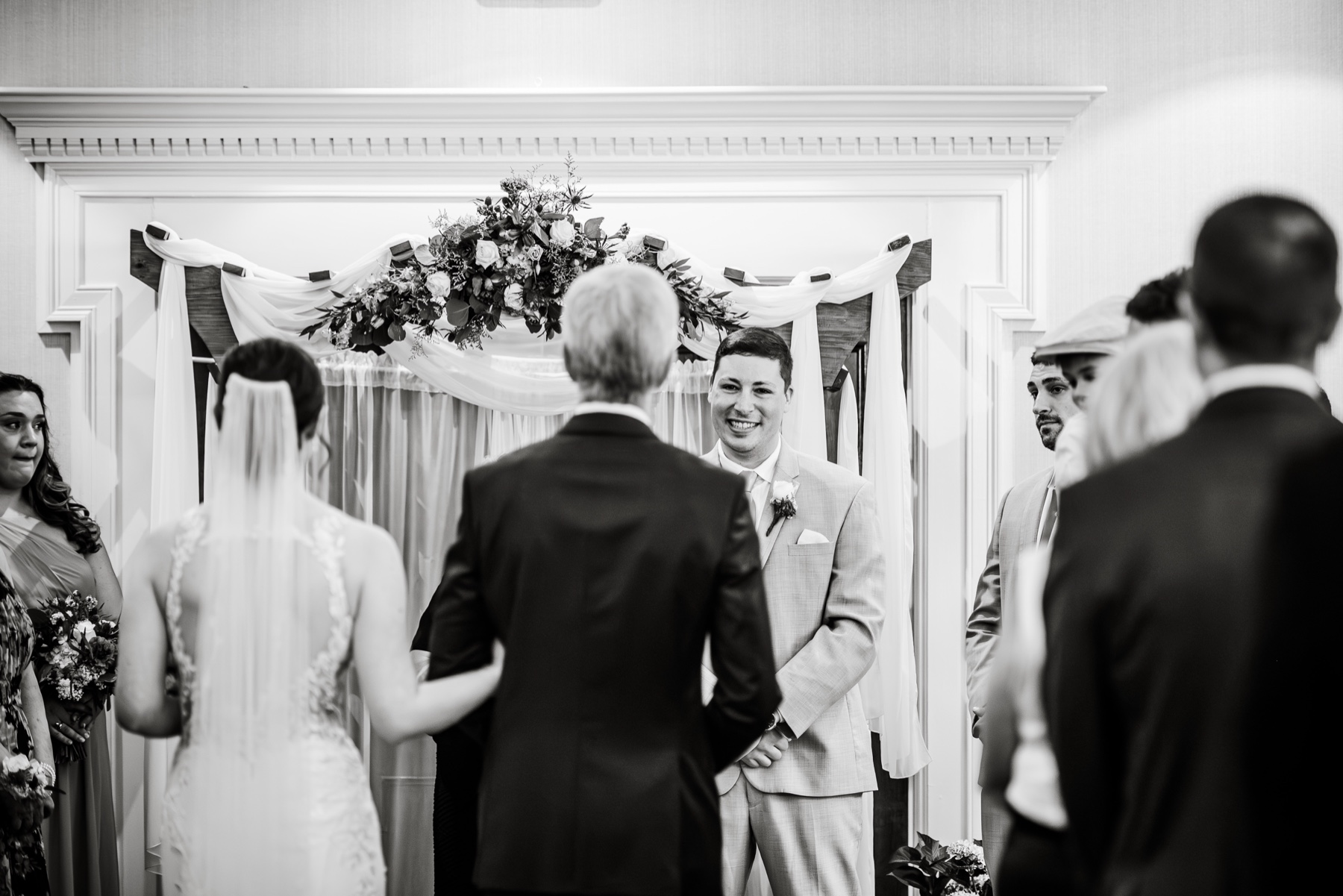 bride walking down the aisle with her father as groom smiles 