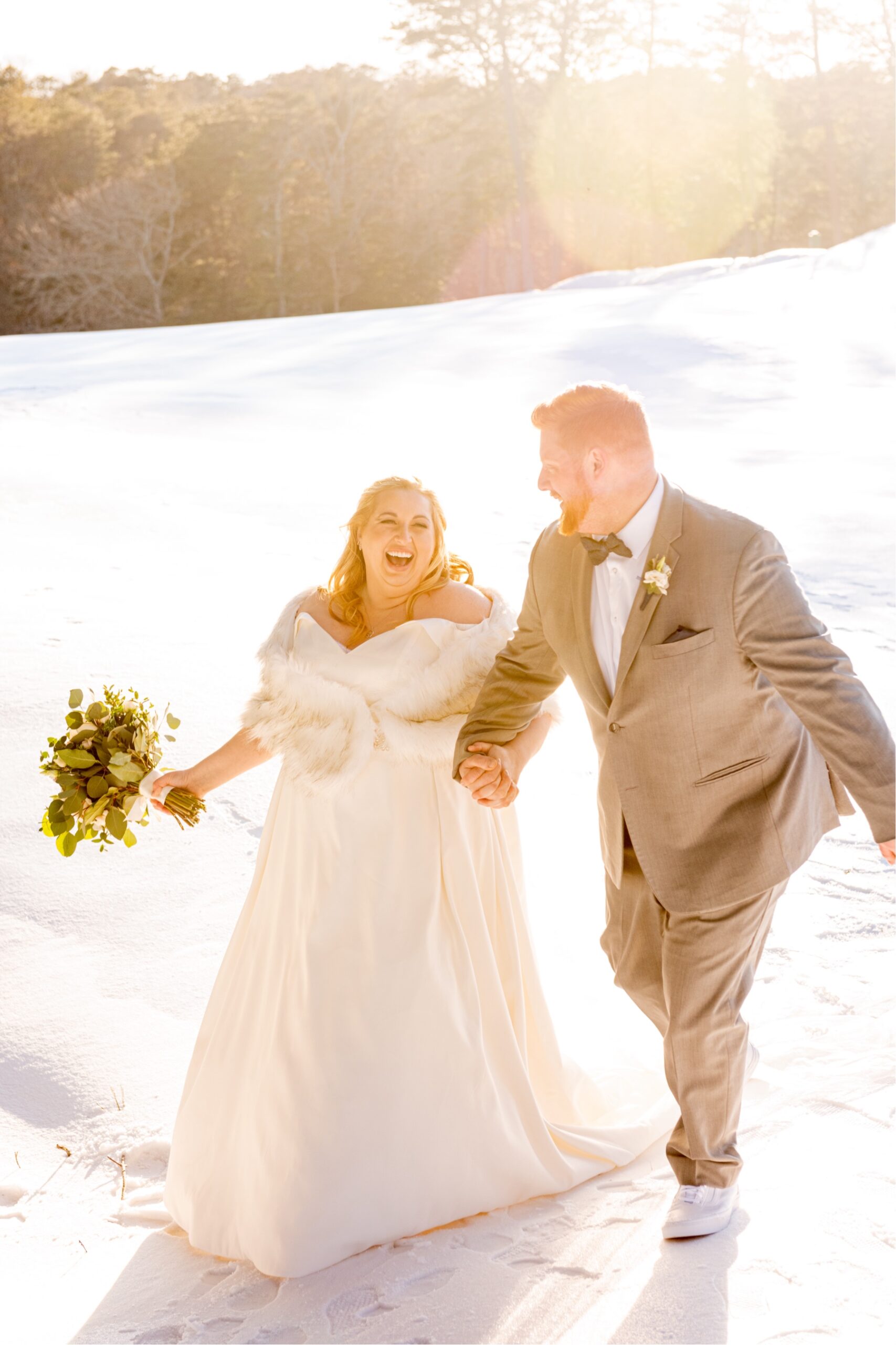 bride and groom walking along snowy field with sunlight behind them